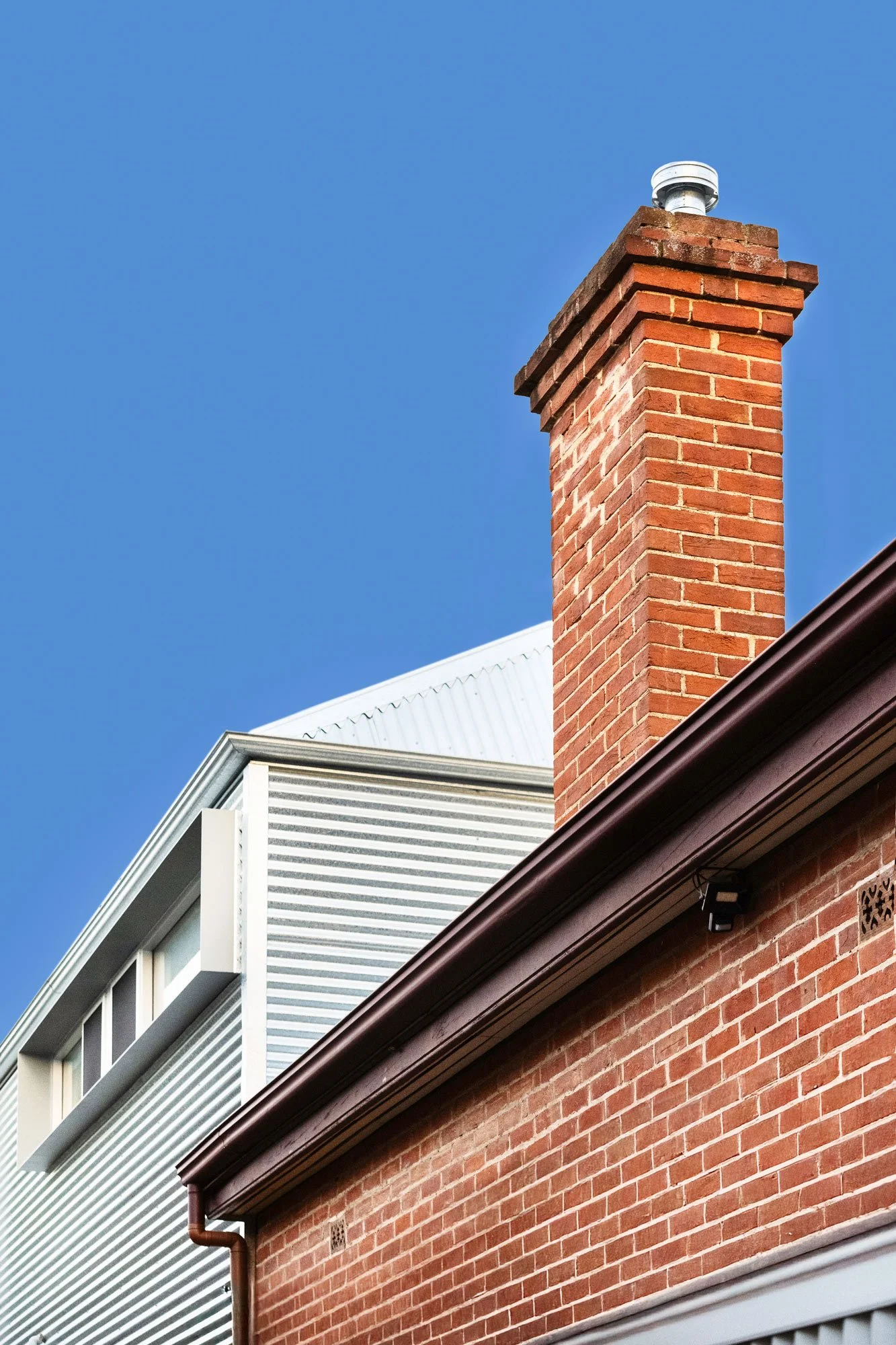 Low-angle view of the roof structure displaying the juxtaposition of the Edwardian brick structure and chimney alongside a modern extension wrapped in corrugated iron.