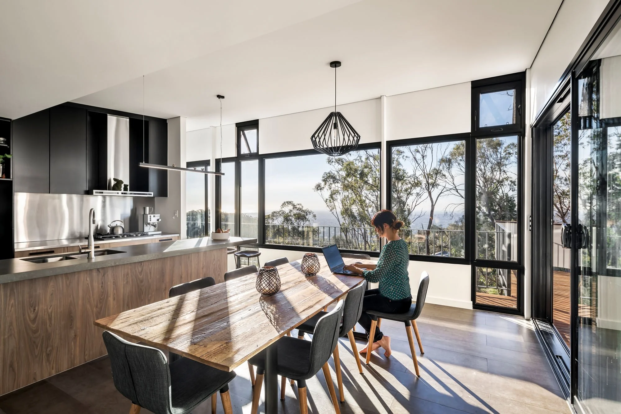 Interior view of the kitchen and dining area featuring floor-to-ceiling windows. The expansive glass showcases a spectacular view of the rugged Australian bush, with the sea visible on the distant horizon.