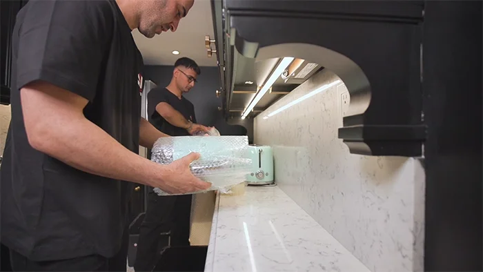 Professional movers carefully wrapping kitchen items and organizing a modern countertop during a residential move in Toronto.