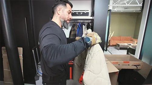 A happy family with two children relaxes on the floor of their new home, surrounded by cardboard boxes and houseplants near a bright window—capturing a peaceful moment during a residential move.