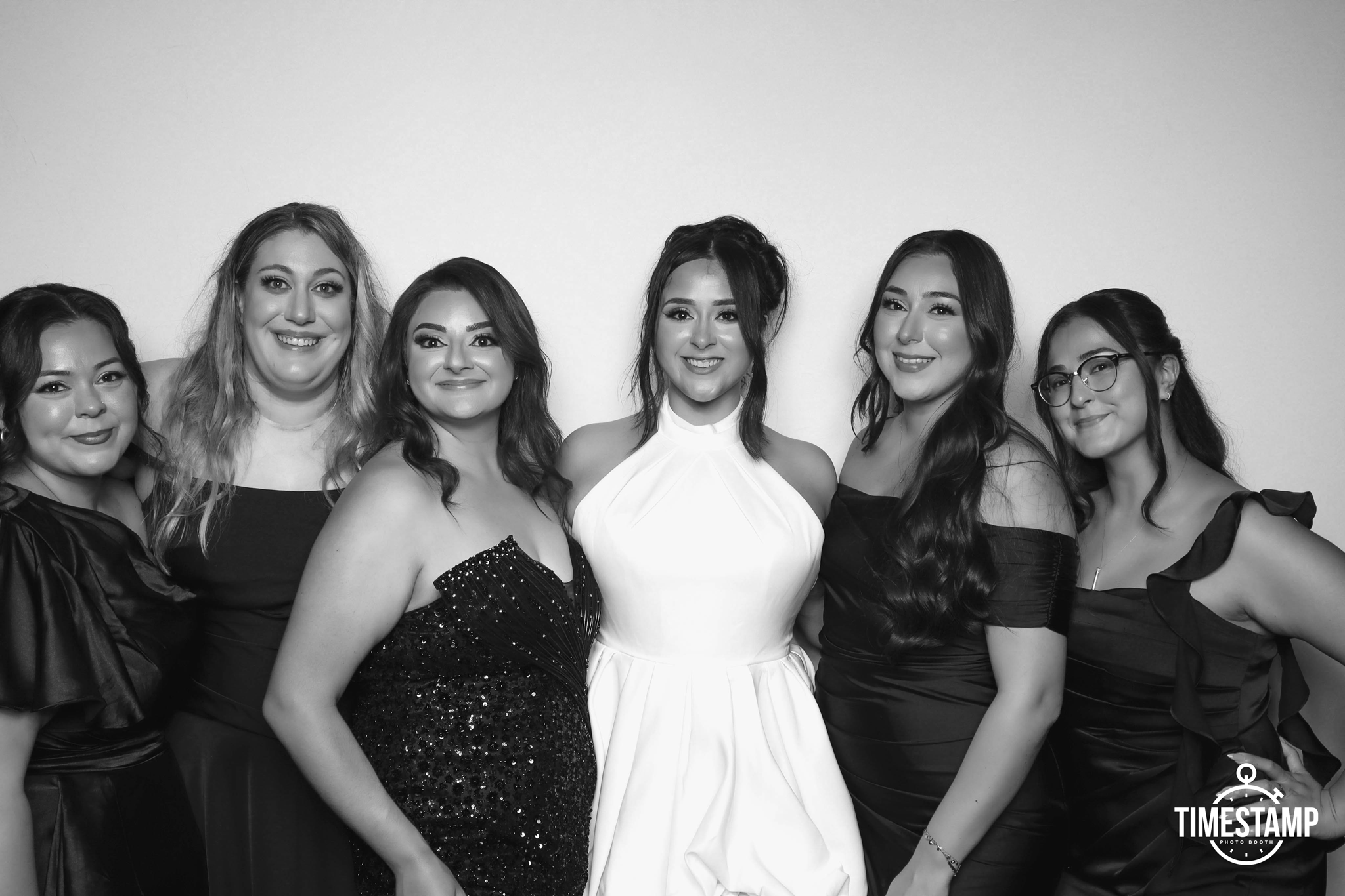 Group of six women dressed in formal attire smiling for a photo in front of a plain wall.
