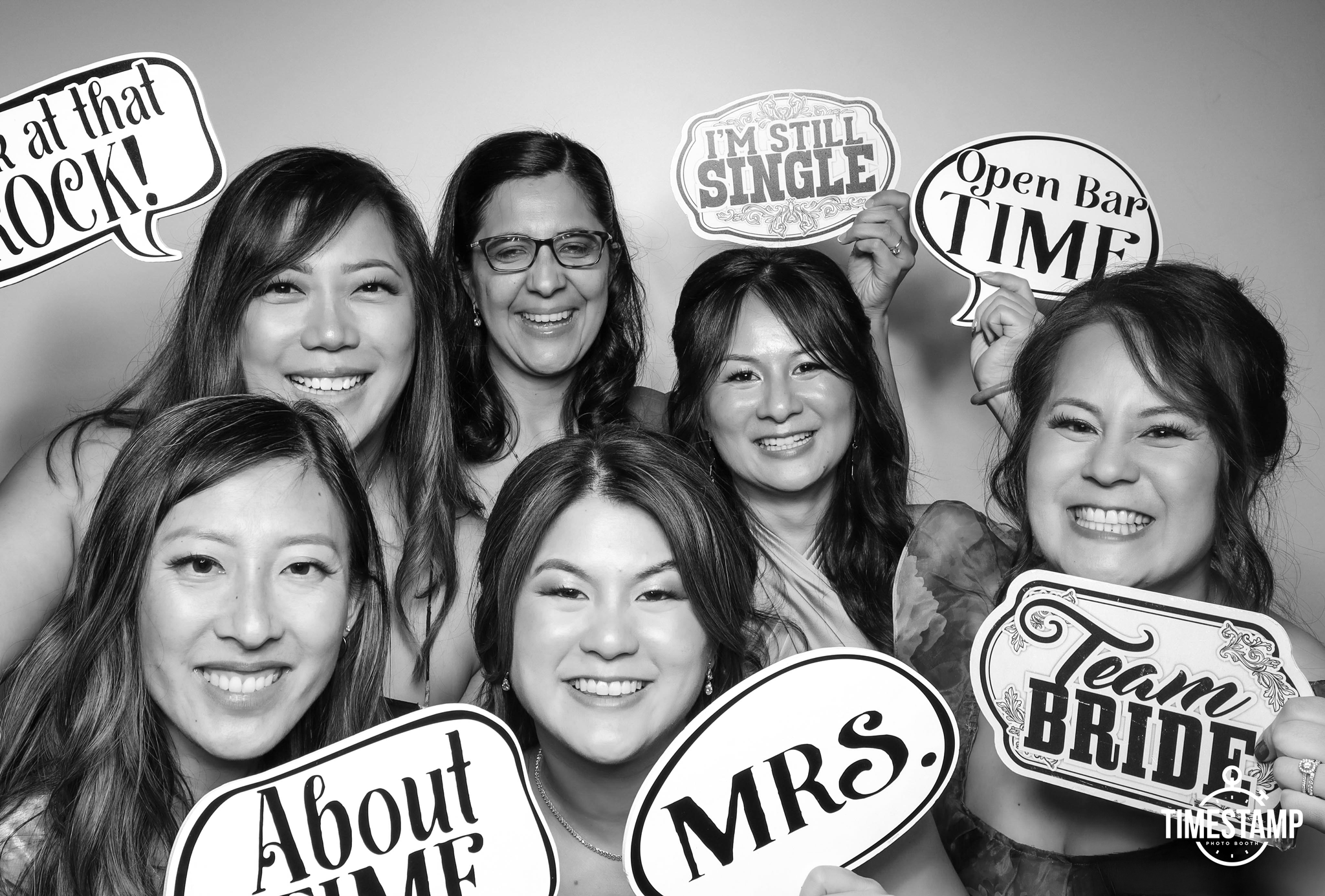 A group of women smiling and holding signs with bridal shower messages, including 'I'm still single,' 'Open bar time,' 'About to get married,' 'Mrs.,' and 'Team bride'.