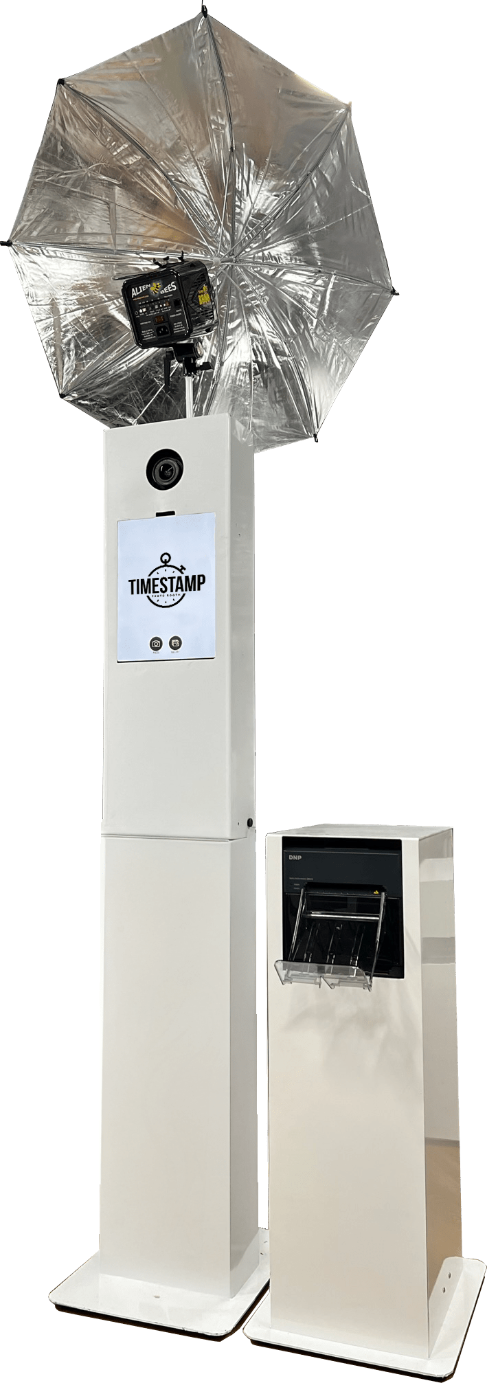 A photobooth setup with a tall white cabinet, a large umbrella with a light, a camera, and a smaller white booth, all against a black background.