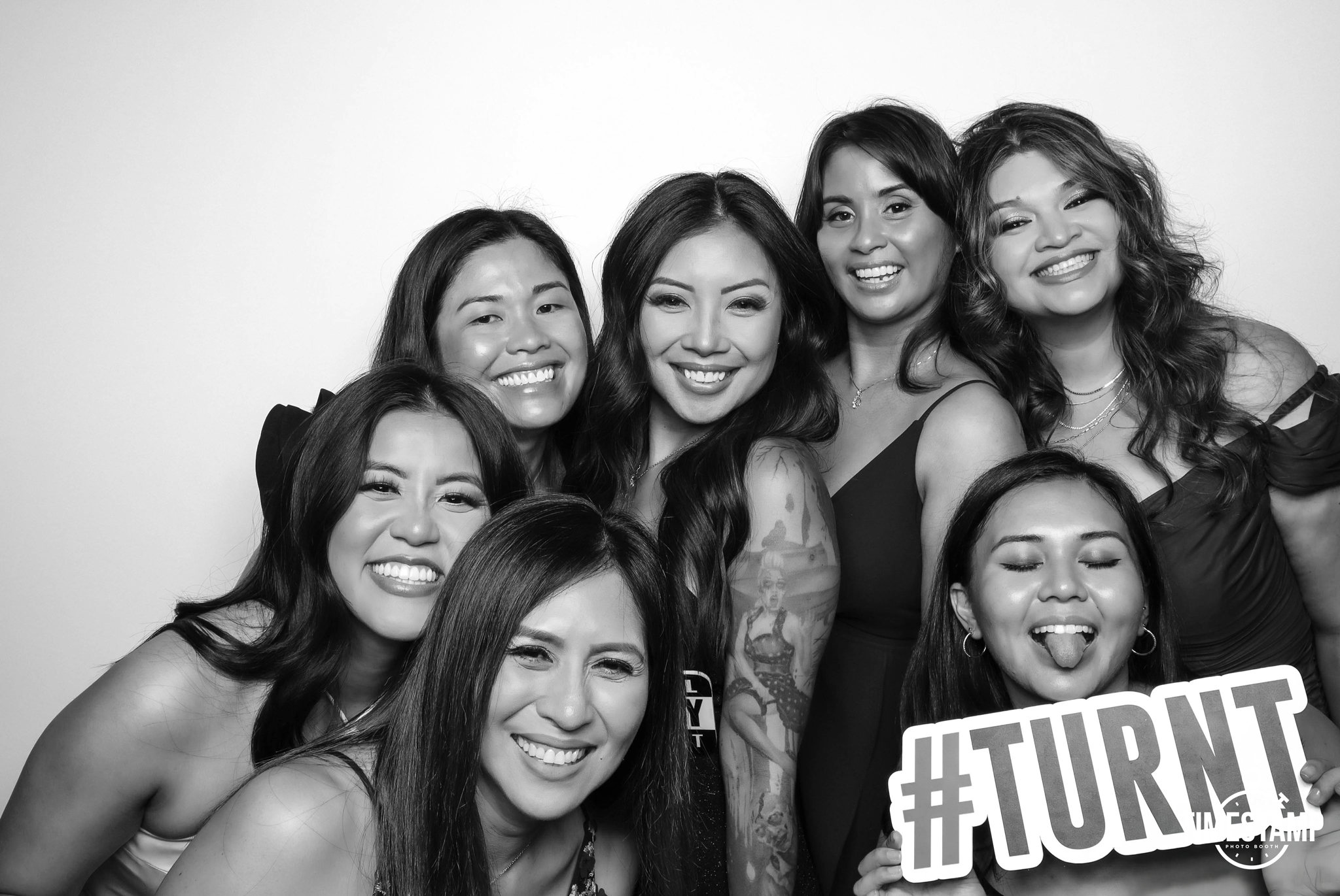 Black and white photo of six women smiling and posing together, one holding a sign that says '#TURN'.
