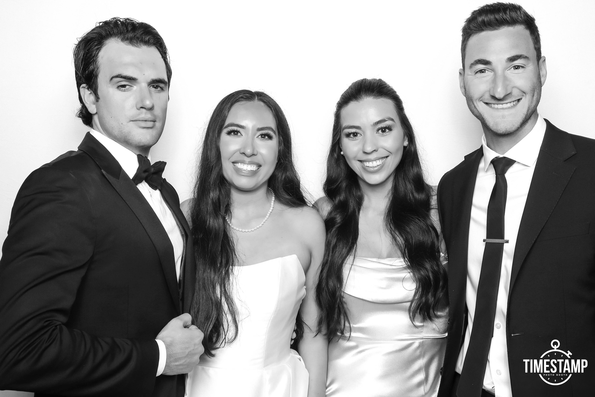 Group of four young adults dressed in formal attire posing for a photo in front of a plain background.