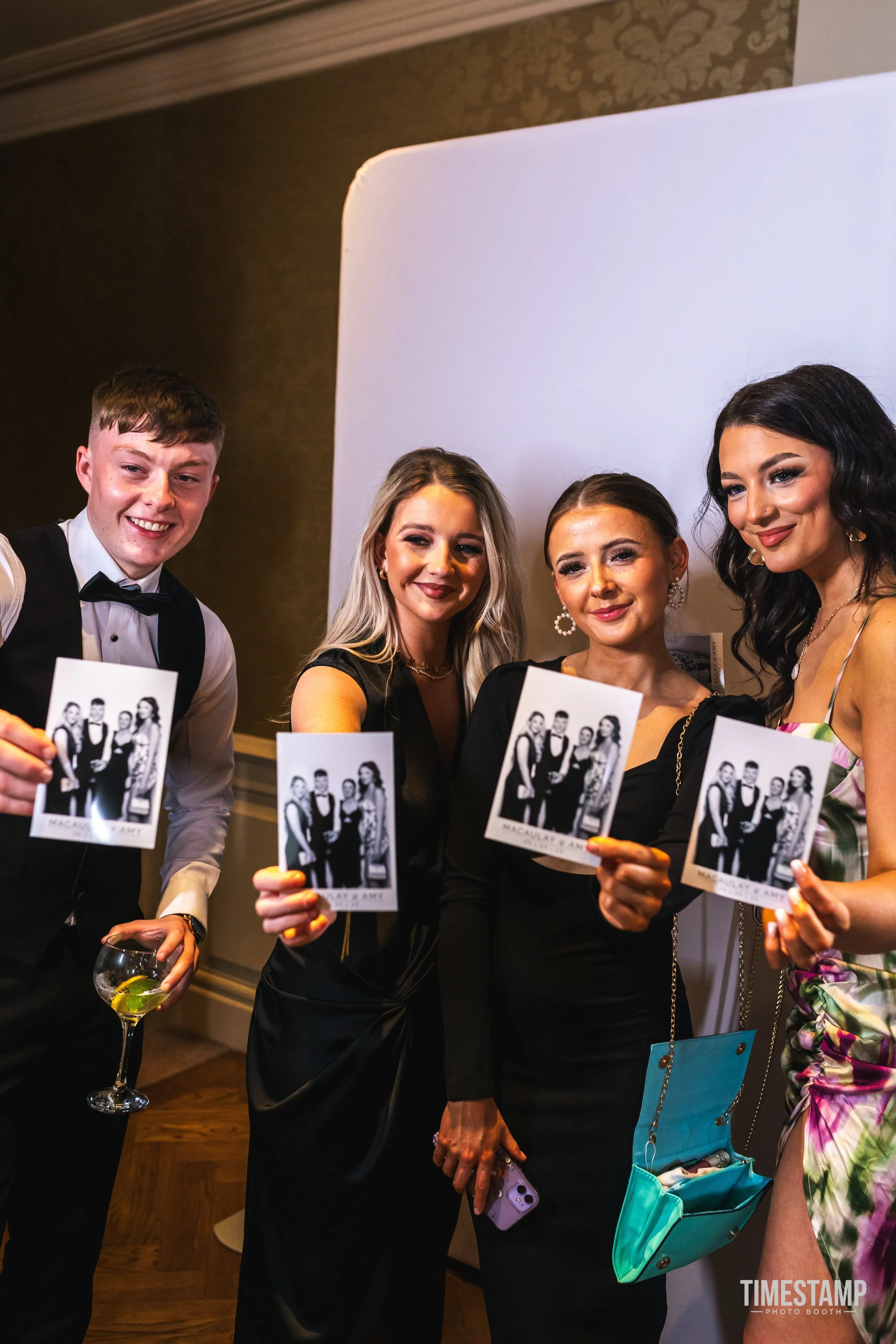 Group of four people in formal attire holding photographs at an event.