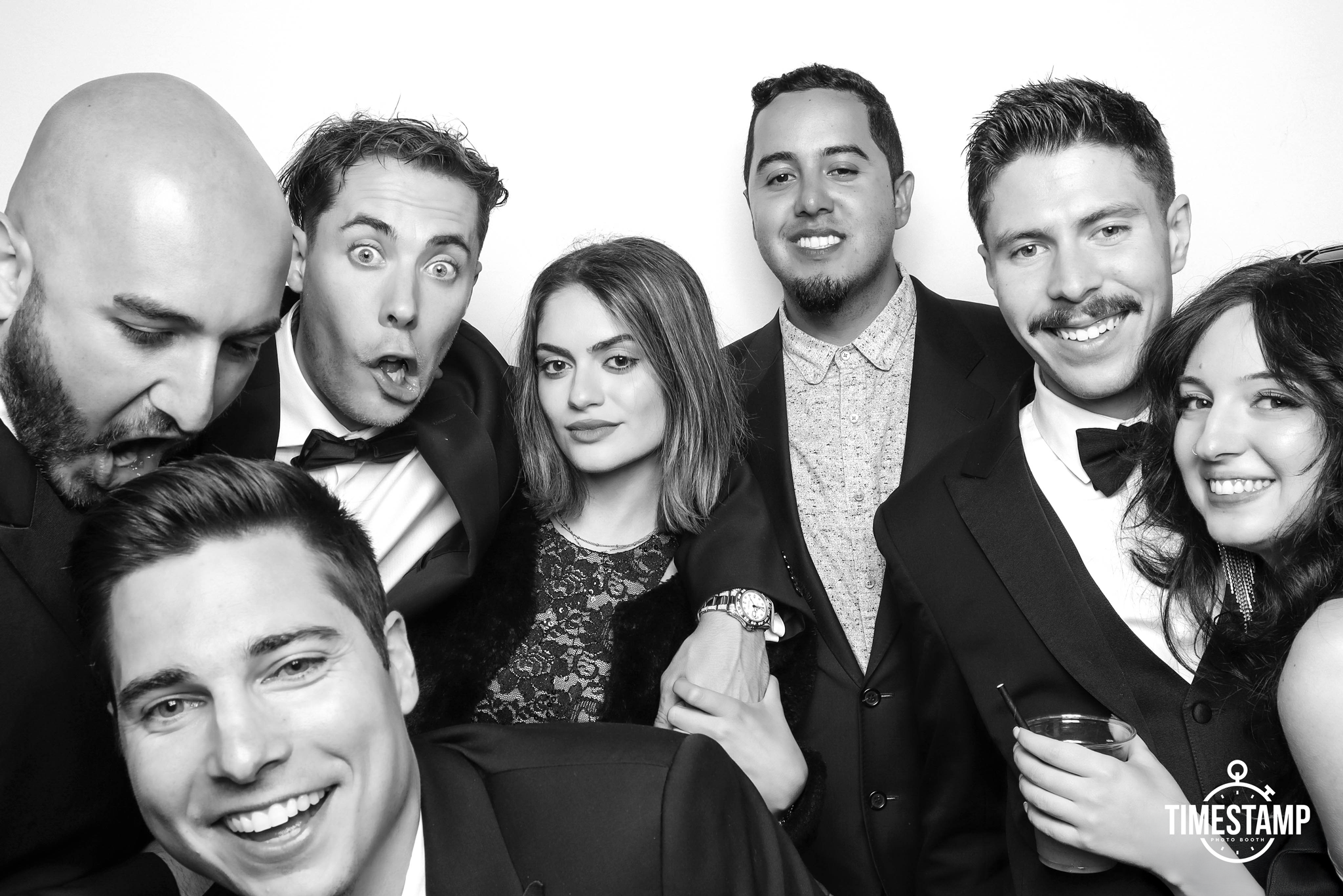 Black and white photo of seven young adults dressed in formal attire at a party or event smiling and posing for the camera.