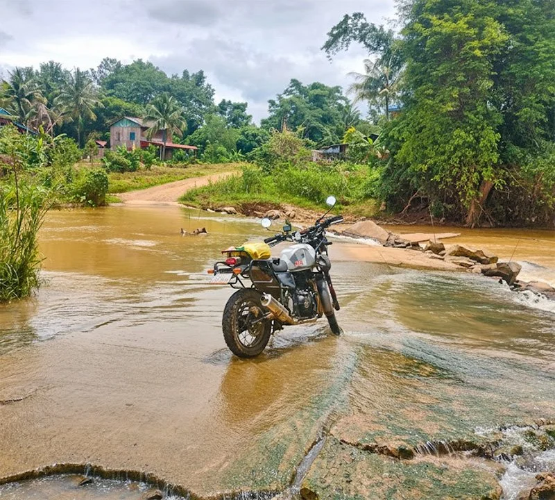 Royal Enfield Himalayan 411 in the middle of a river crossing in the Cambodian mountainous countryside.