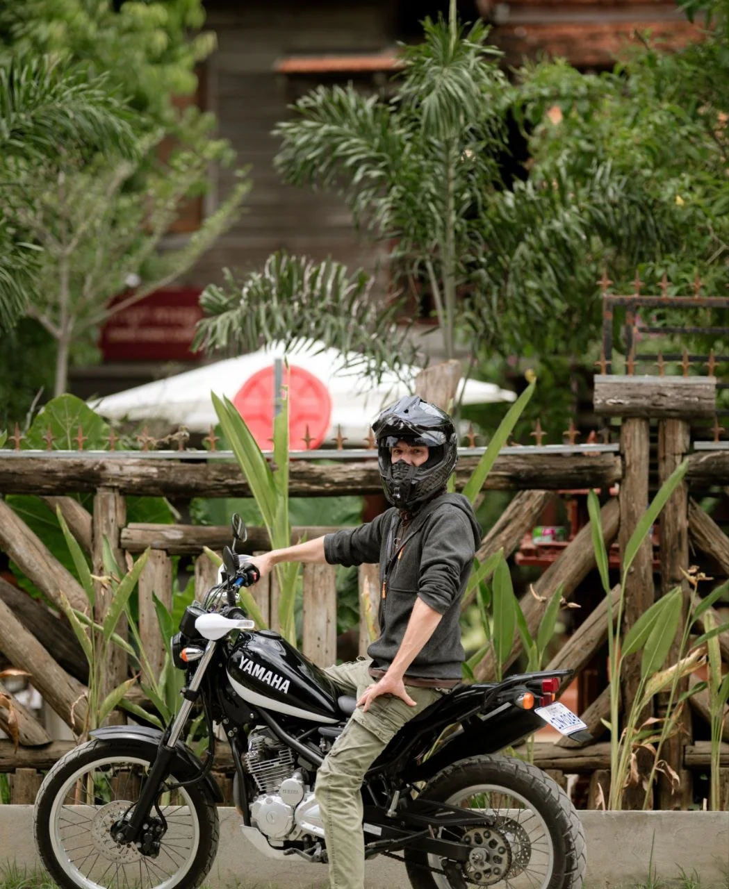 Yamaha Tricker 250 Tricker with a rider posing for the camera with a green natural background with a wooden house in Cambodia.