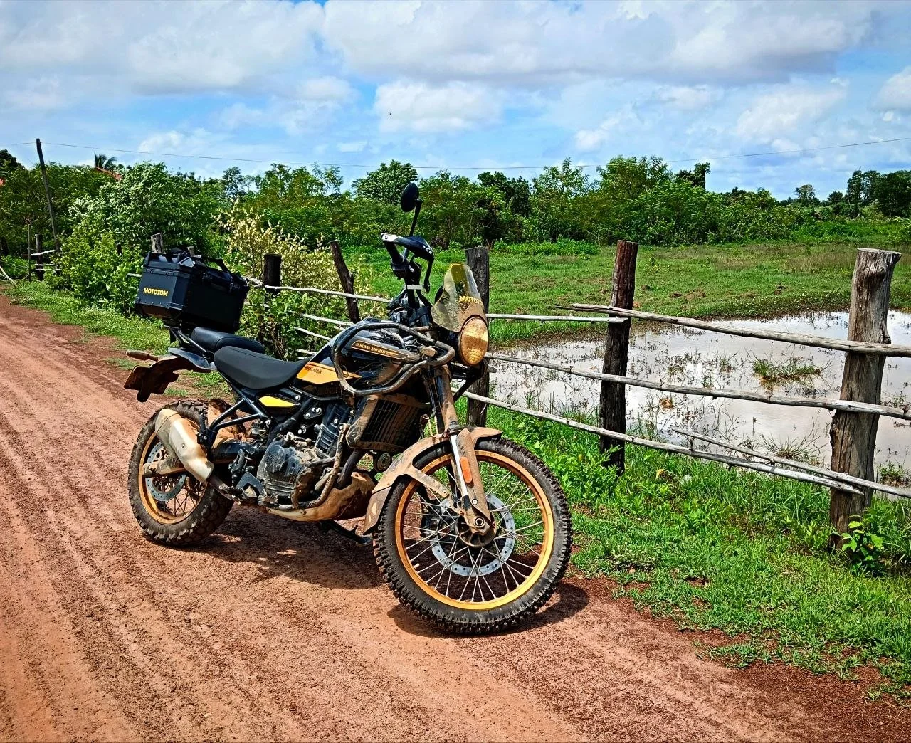 Black Royal Enfield Himalayan adventure motorcycle with accessories on a dirt road near a lake in Preah Nimith, Cambodia.