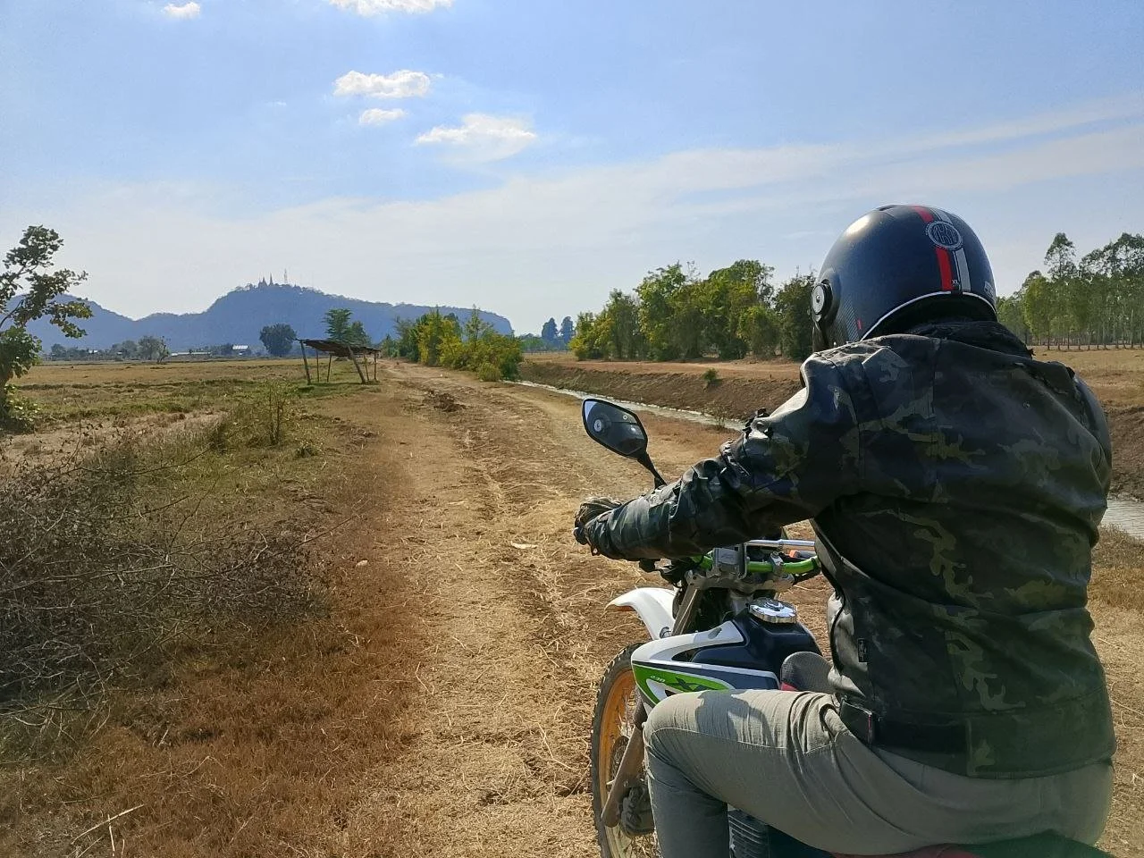 View of Phnom Sampov in Battambang from a rider on a motorbike on a dirt trail along a canal.