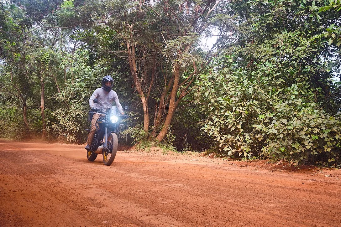 Rider standing up, riding on a red dirt road with trees.