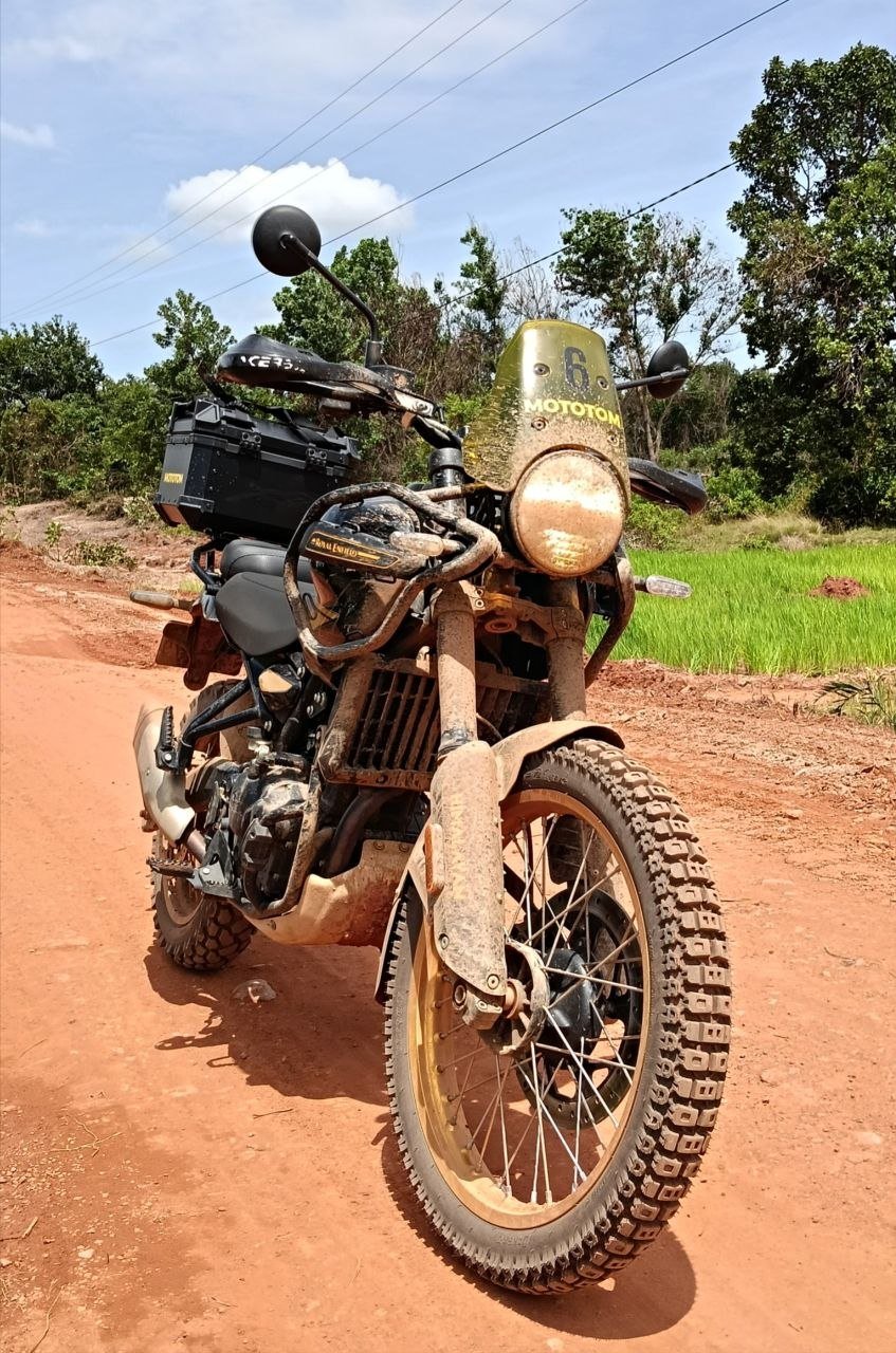 Muddy Royal Enfield Himalayan motorbike on a dirt road in the Cambodian wild.