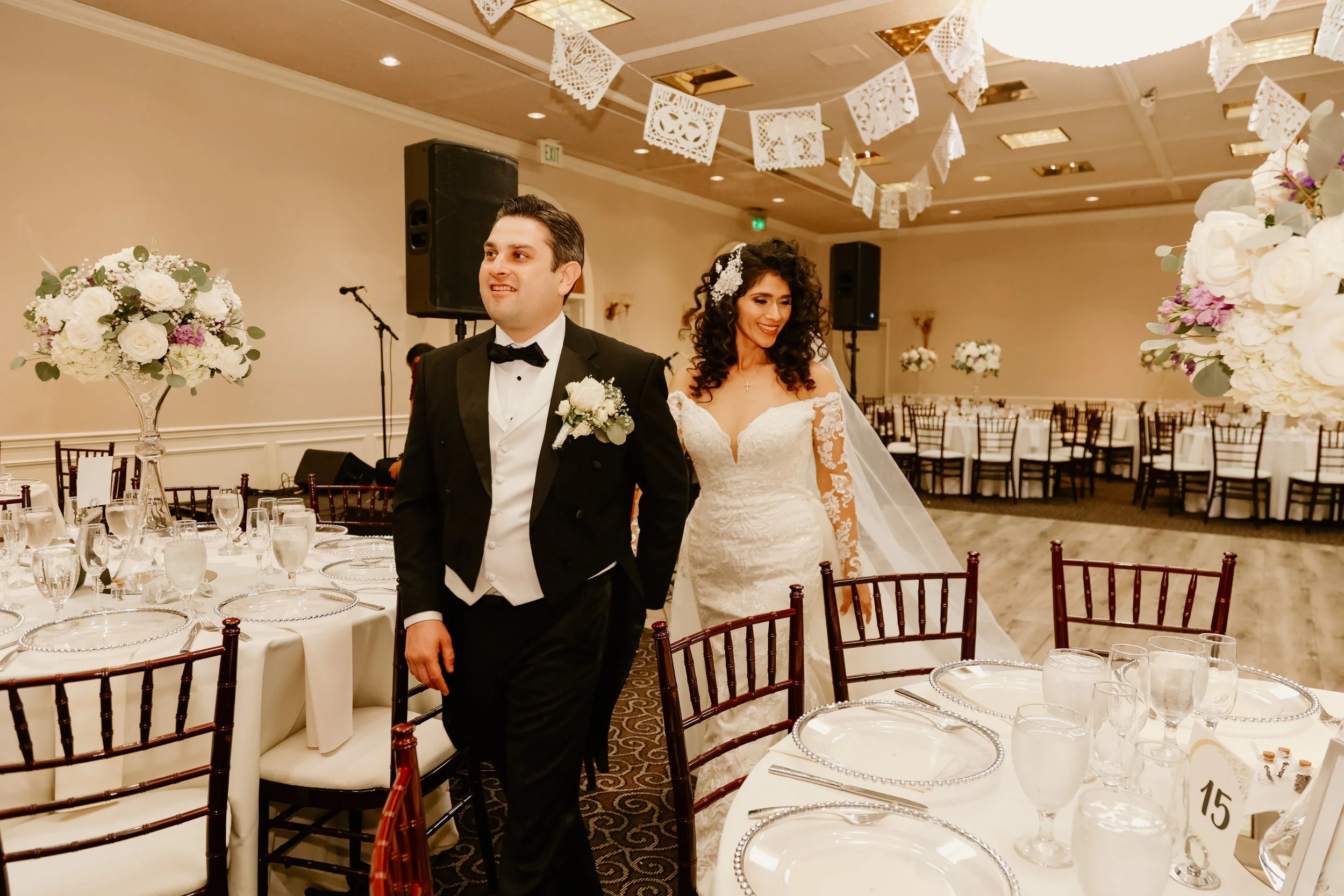Bride in floral gown and groom in suit embracing outdoors, grass background
