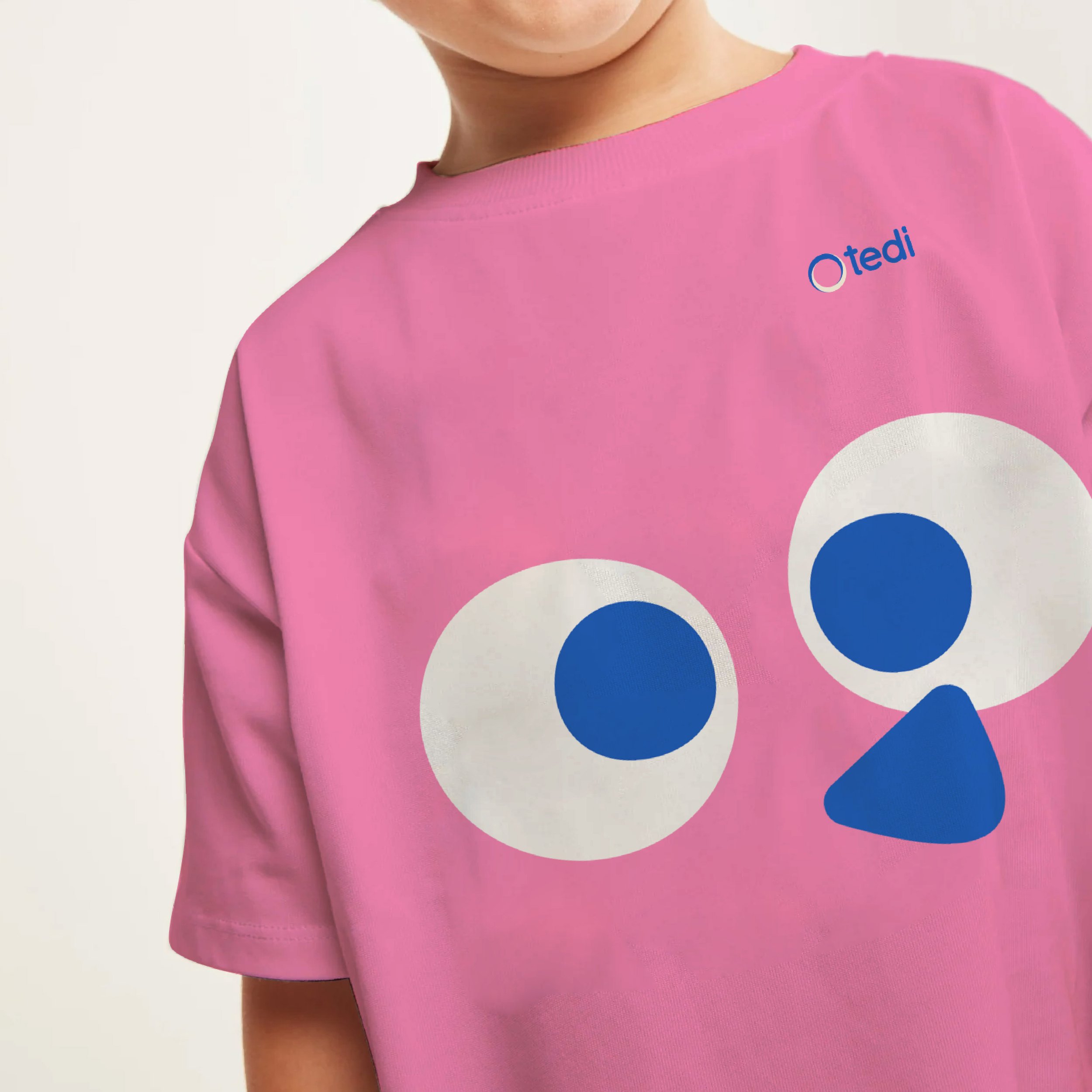 Close-up of a person wearing a pink T-shirt with a tedi on the chest. The logo has the word 'tedi' in lowercase blue letters inside a pink circle. Tedi vanguardia en sindrome de down