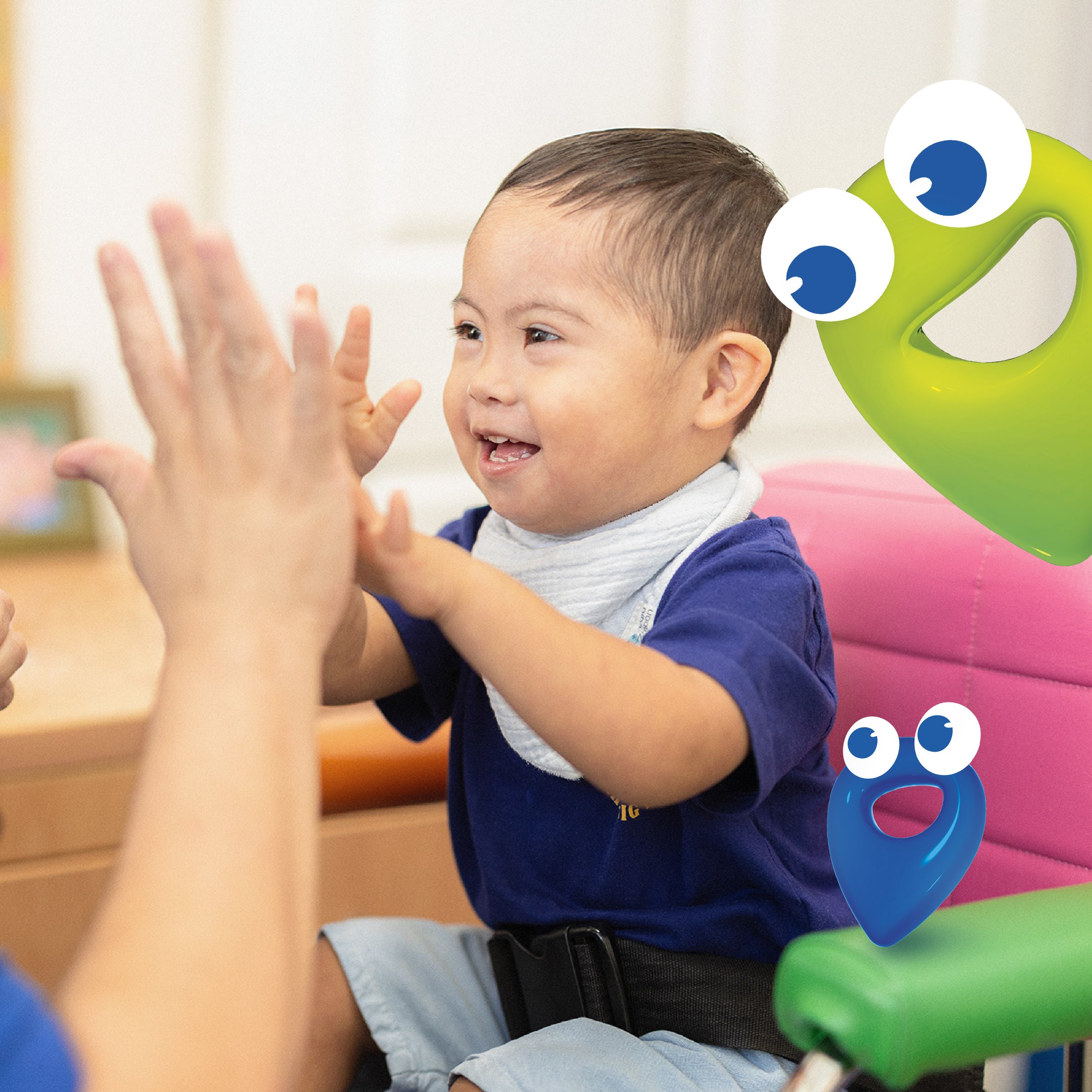 A young boy with short brown hair is engaging with a green location pin with large eyes. The boy has a joyful expression and is wearing a blue shirt with a white collar and light blue shorts. Tedi vanguardia en sindrome de down