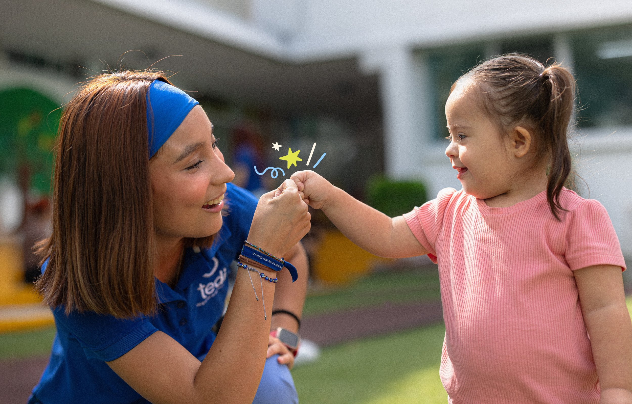 A young girl and a woman smiling and touching fists face-to-face outdoors. Tedi vanguardia en sindrome de down