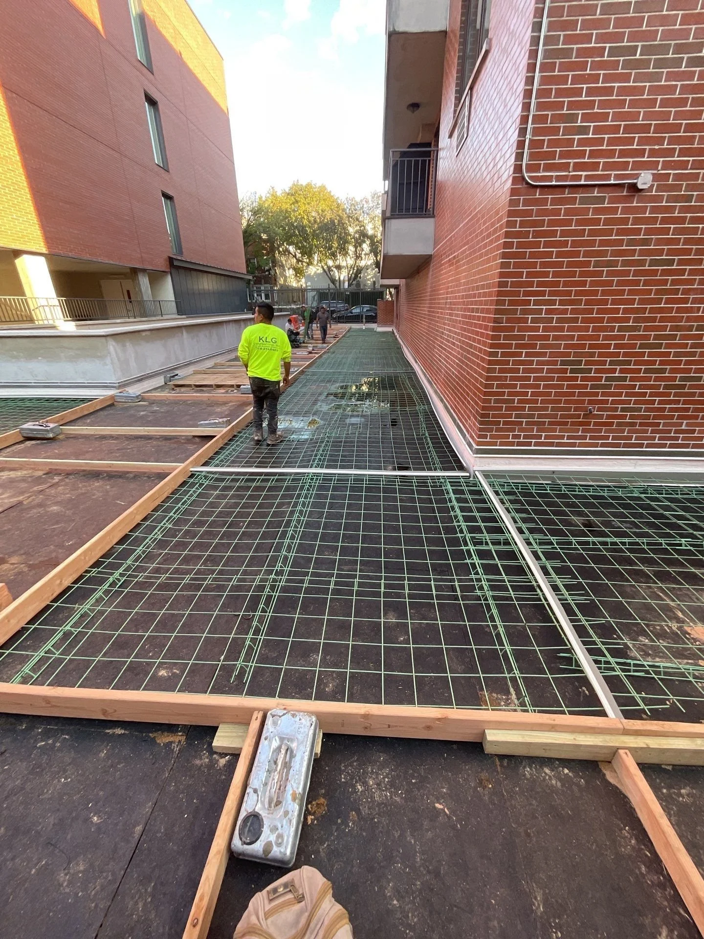 Construction workers installing a grated surface on a rooftop, with wooden framing and city buildings in the background.