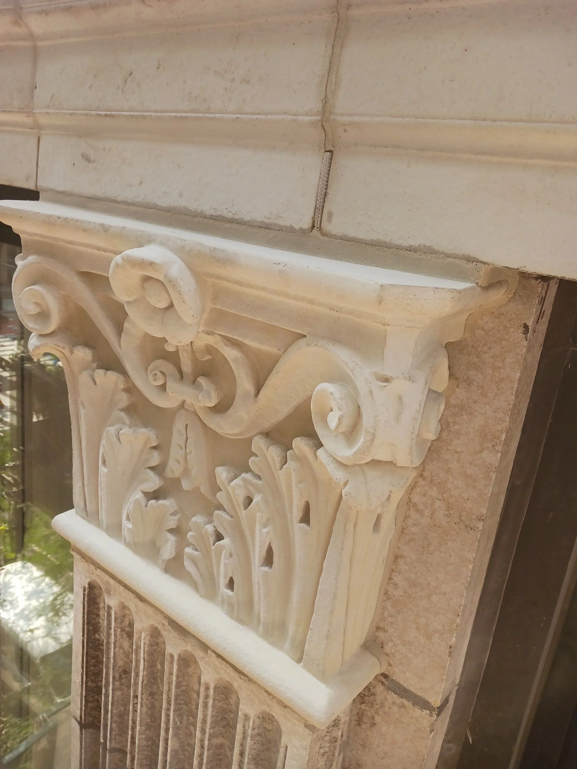 Close-up of decorative architectural stone or concrete corbel with intricate floral and scroll carvings on a building exterior.