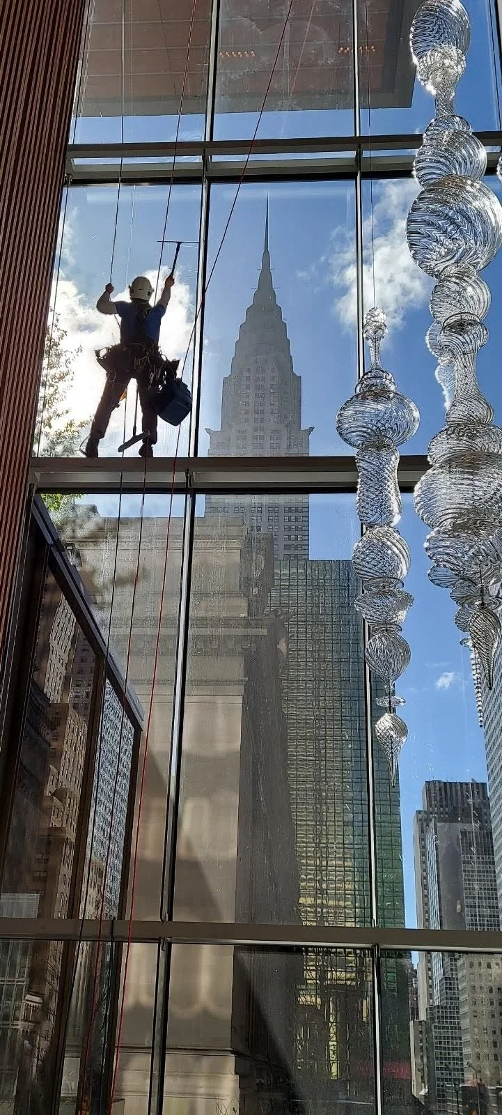 Worker cleaning large glass windows inside a modern building, with the Empire State Building visible through the window.