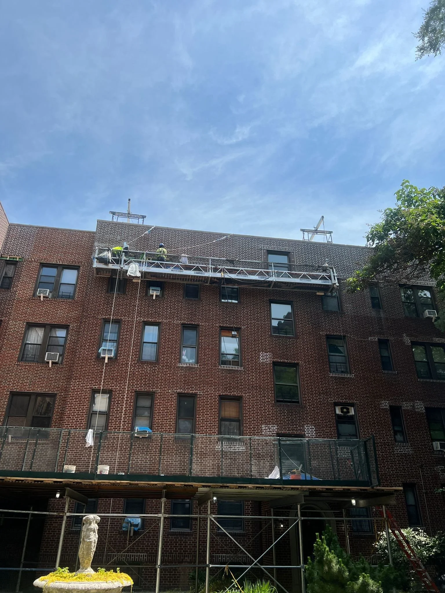 Construction workers on scaffolding working on the exterior of a brick apartment building on a sunny day.