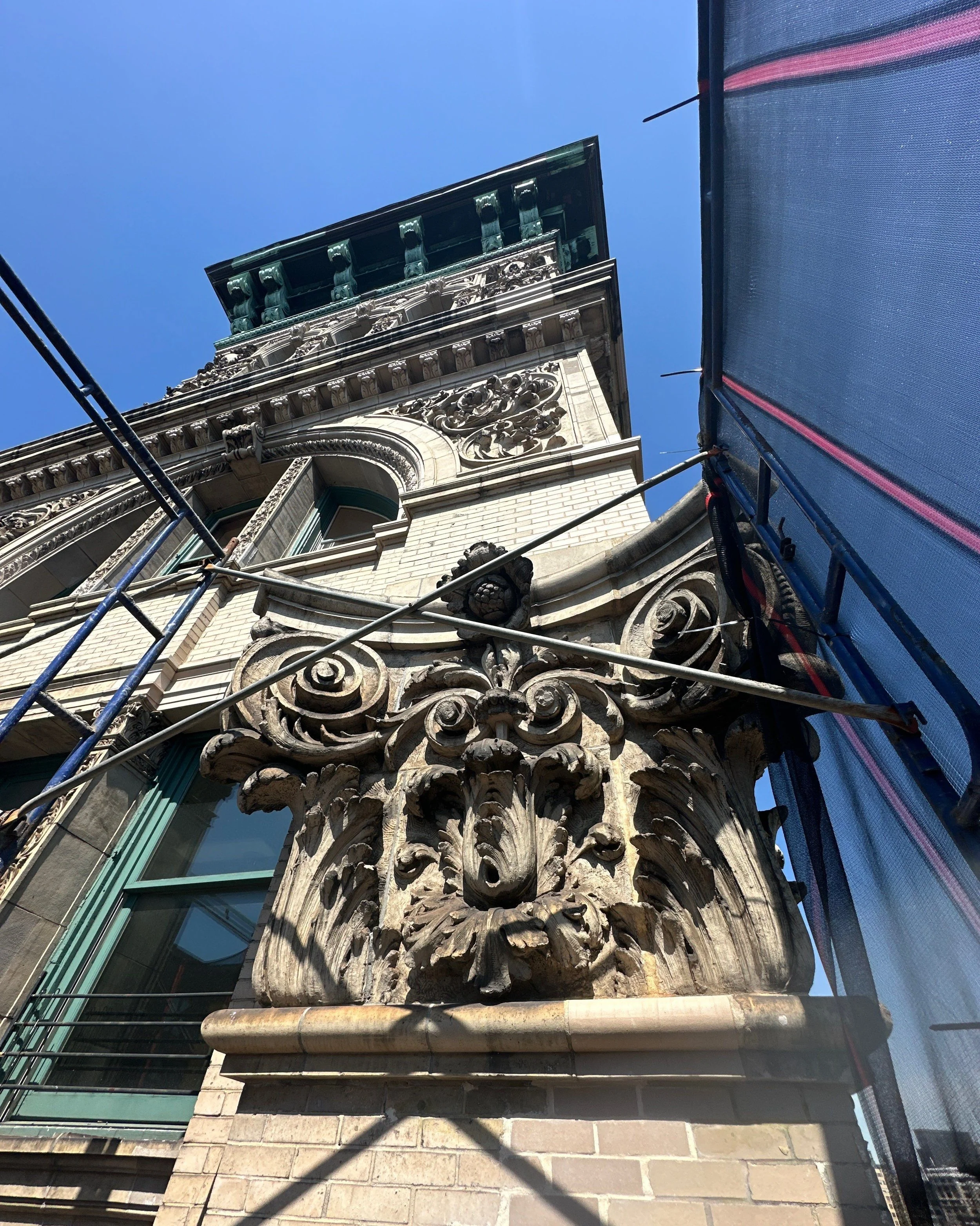 Detailed architectural stone carving on a building with scaffolding and a blue sky.