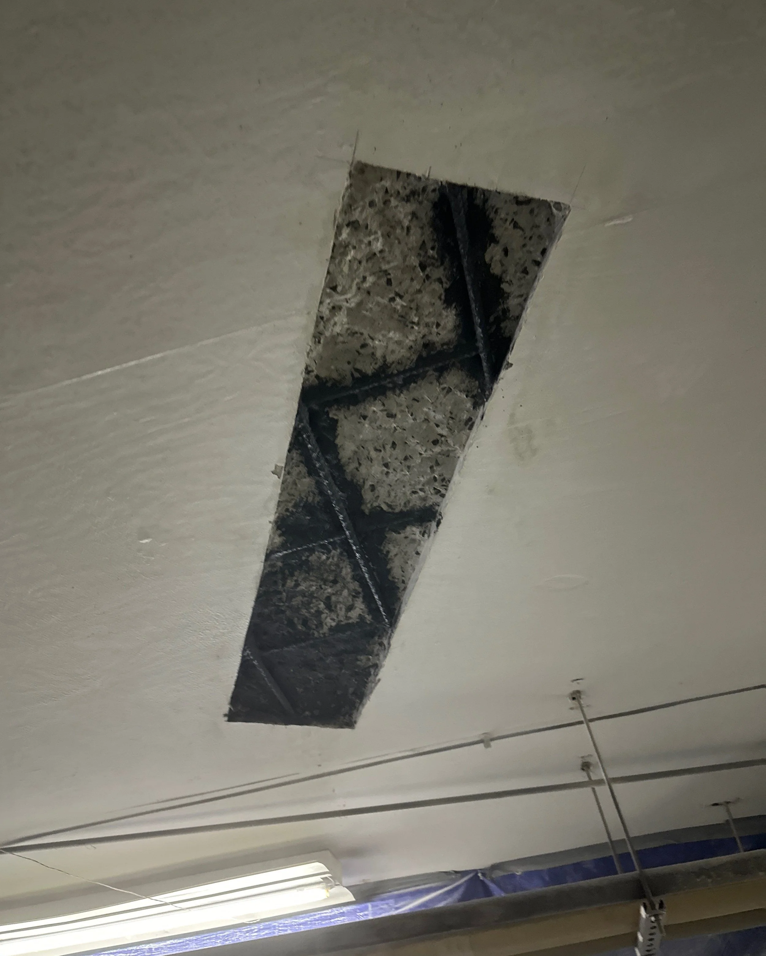 Ceiling with cutout revealing exposed pipes and steel reinforcements.