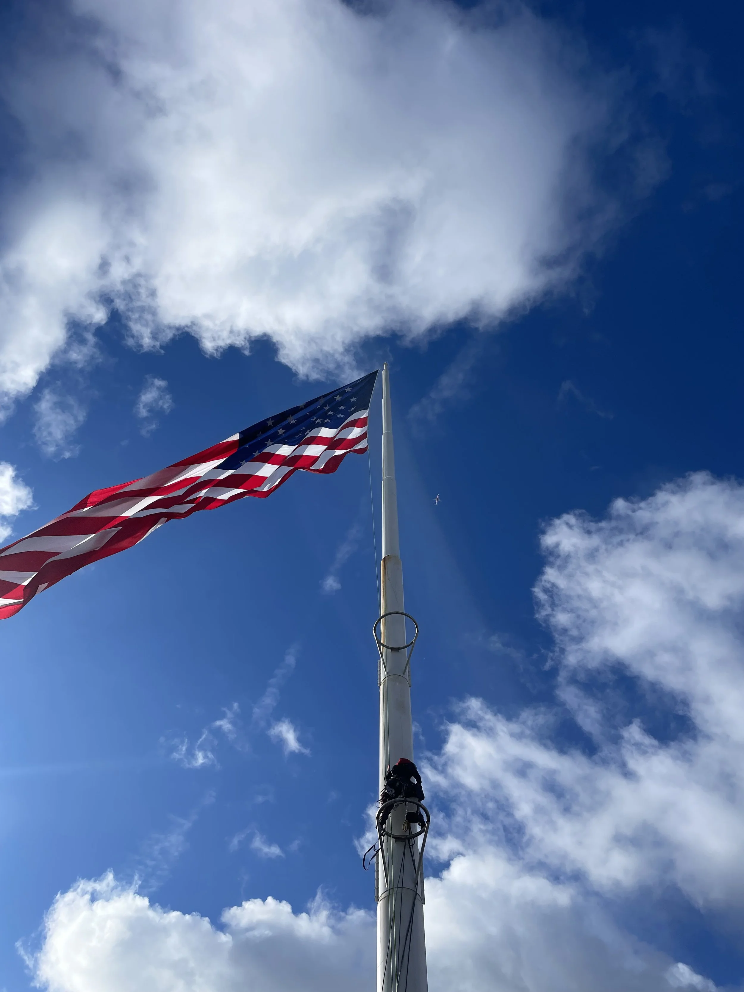 An American flag flying on a tall flagpole against a partly cloudy blue sky.
