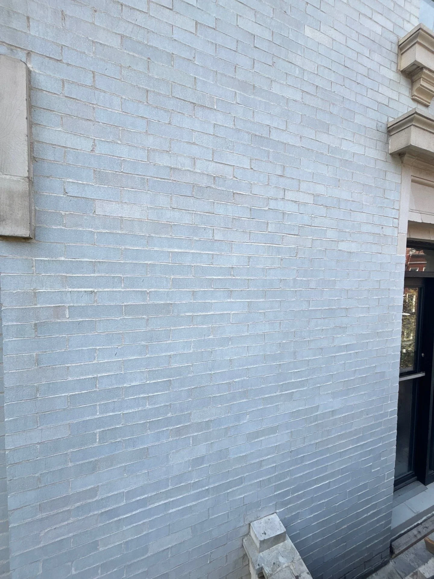Close-up of a light blue brick exterior wall of a building with beige architectural details and a window to the right.
