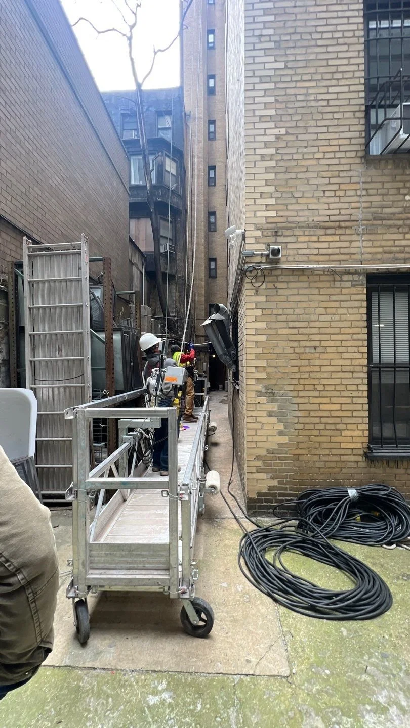 Workers with safety helmets using equipment on a mobile platform in an alleyway between high-rise buildings.