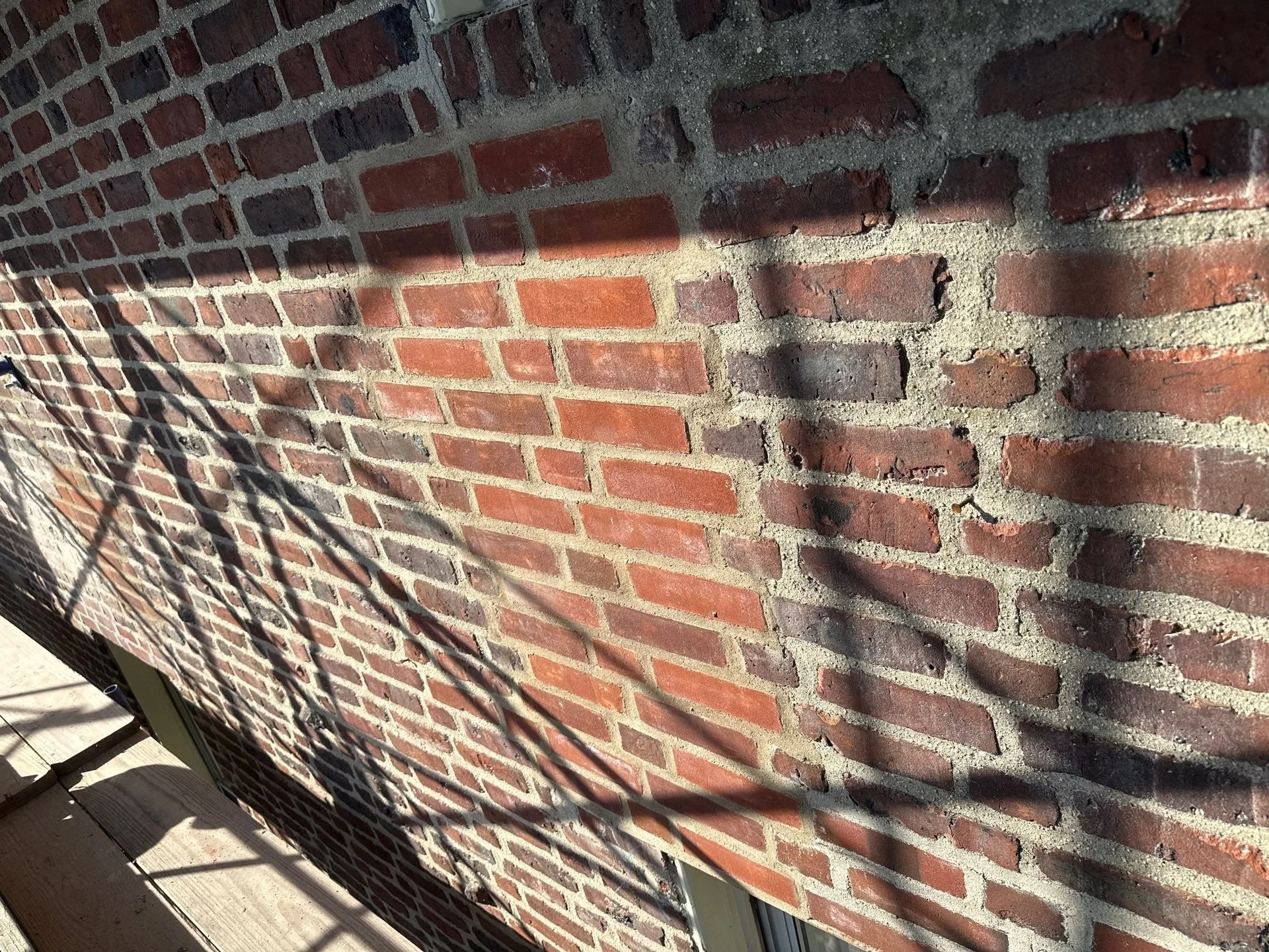 Close-up of a red brick wall with visible mortar lines and shadows cast on it, with a wooden surface at the bottom.