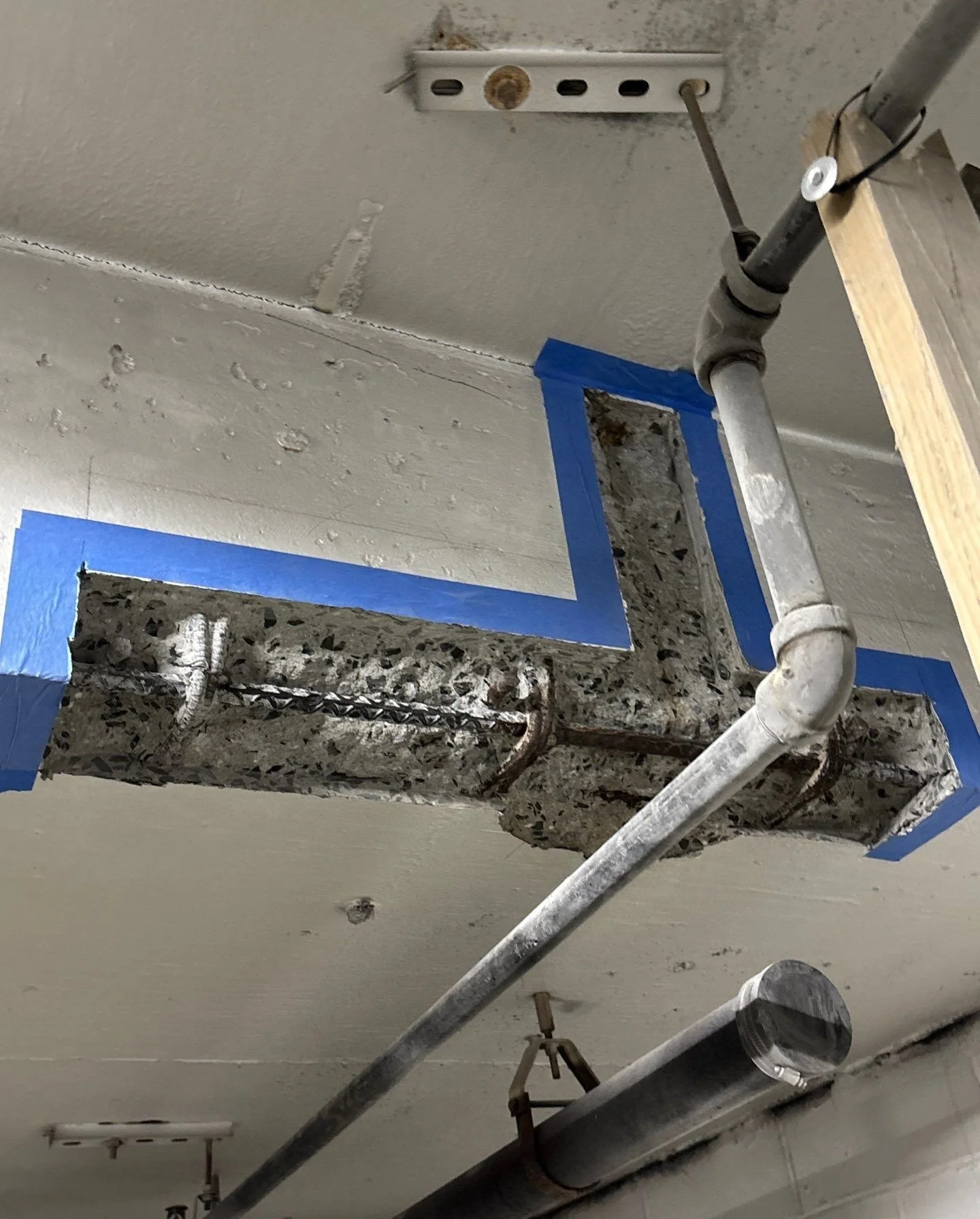 Ceiling with an opening framed with blue painter's tape, exposing pipes and insulation, and a metal support structure.