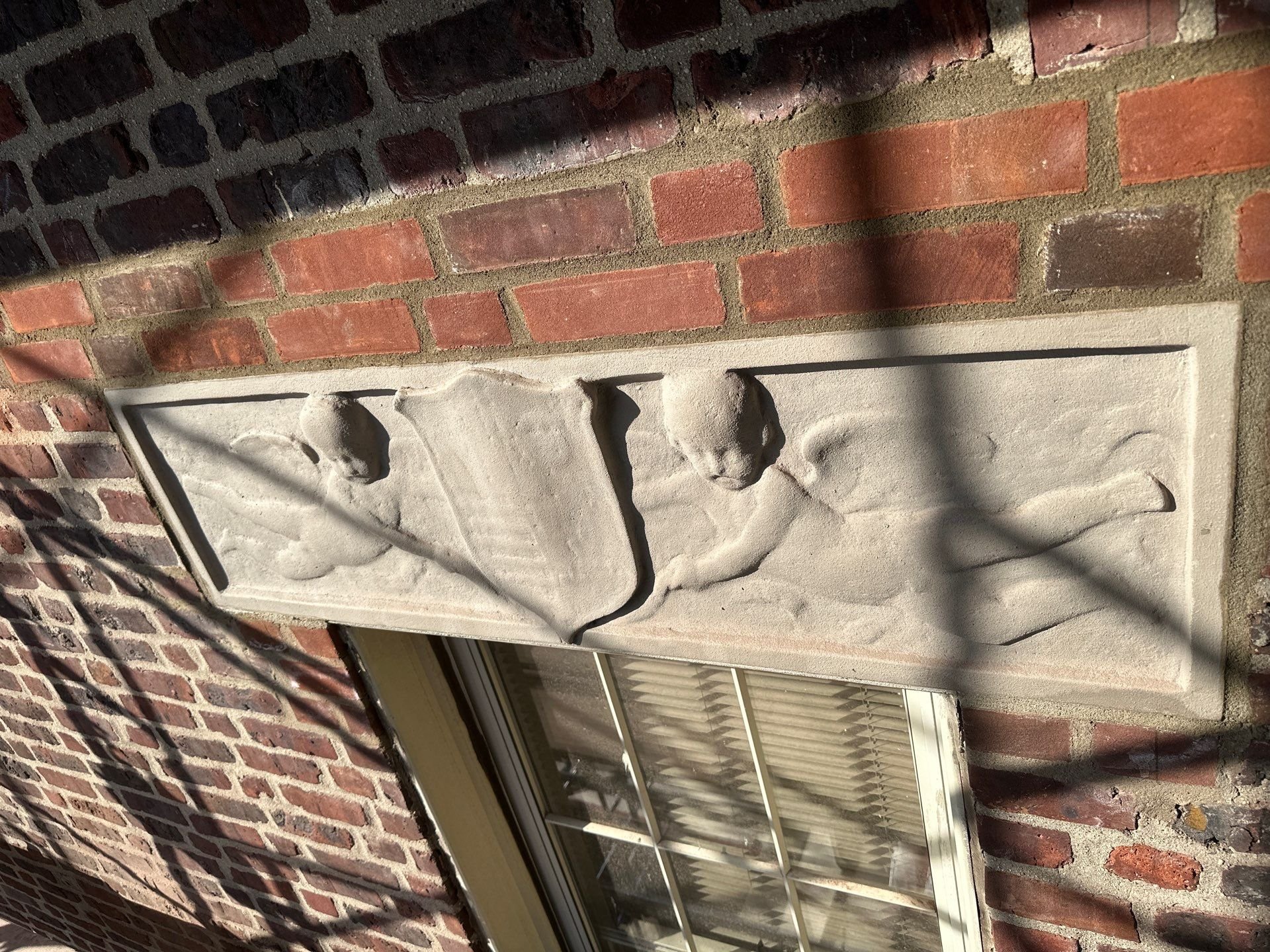 Precast ornamental cast  carved into a rectangular stone plaque mounted on a brick wall on a historical building in Queens, NY. 