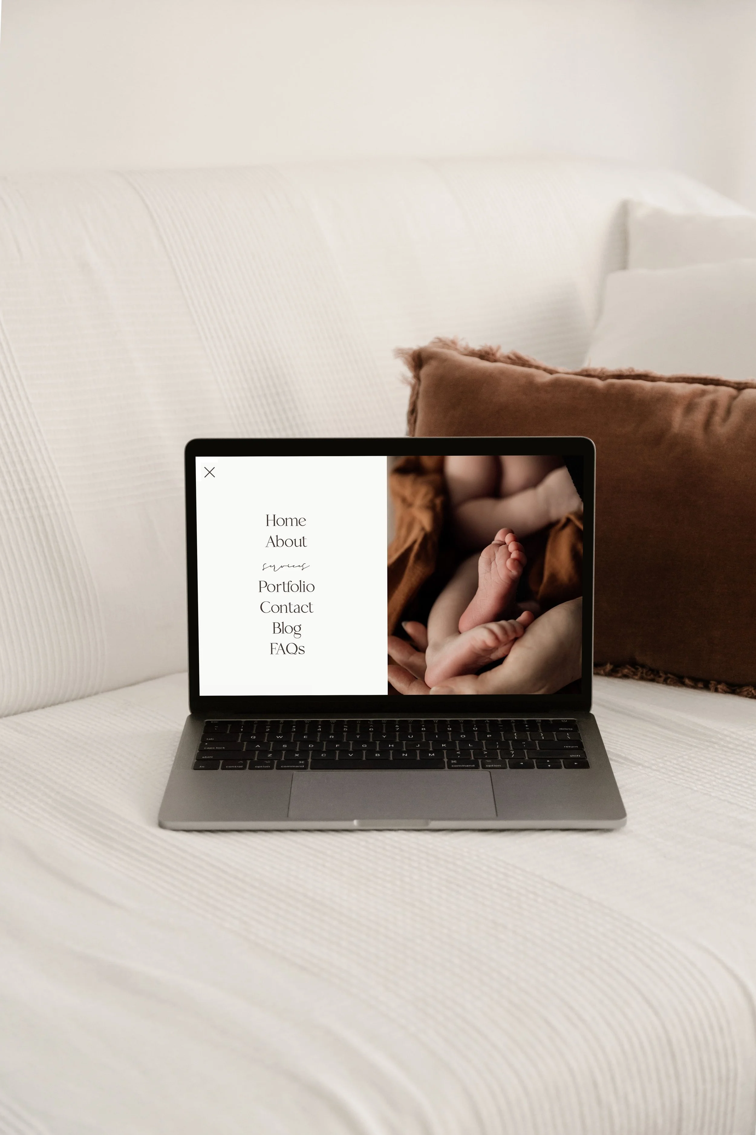 A laptop on a white bed with a website showing a baby photo and a navigation menu on the screen.