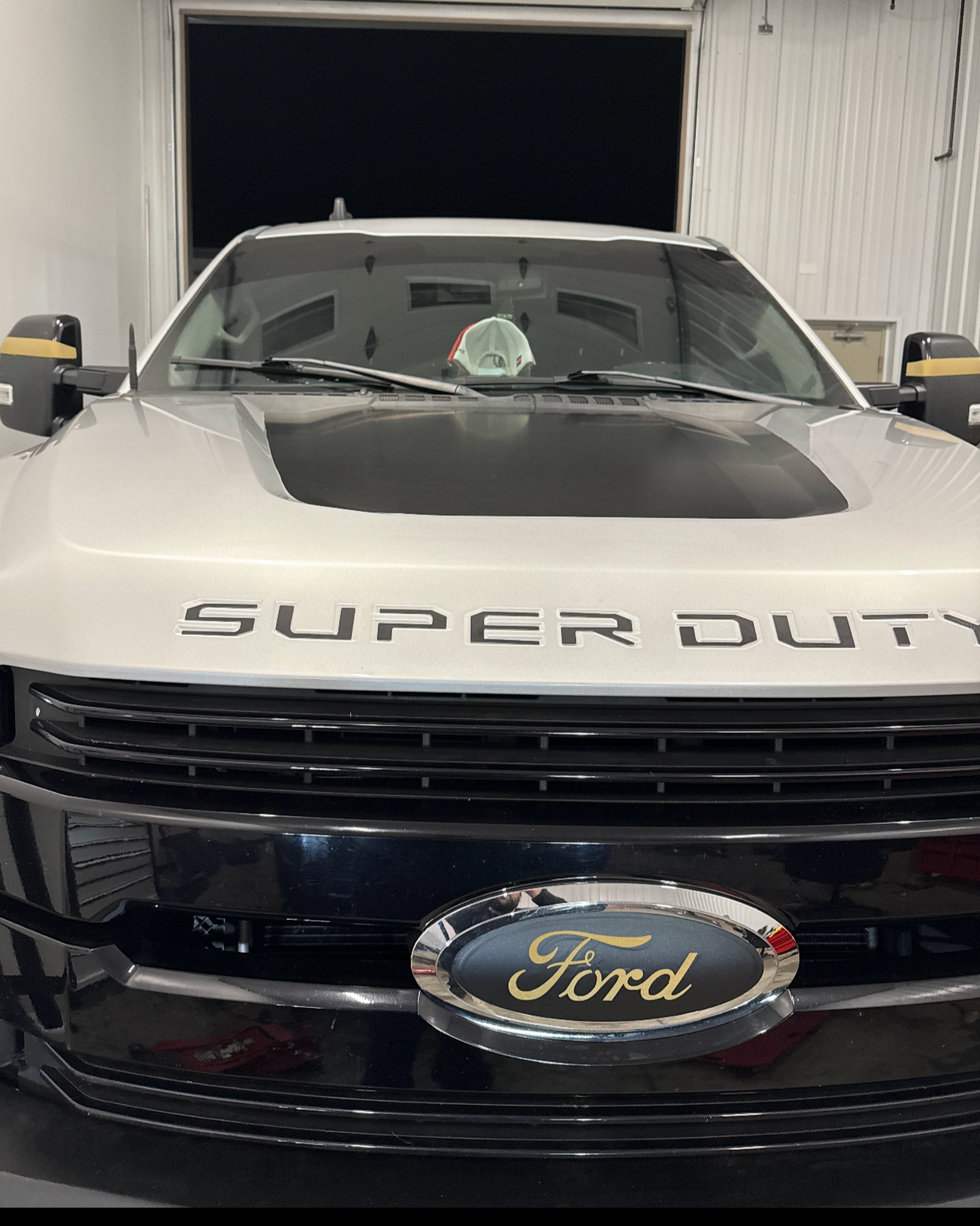 Front view of a Ford Super Duty truck with a black grille and a Ford emblem, parked in a garage.