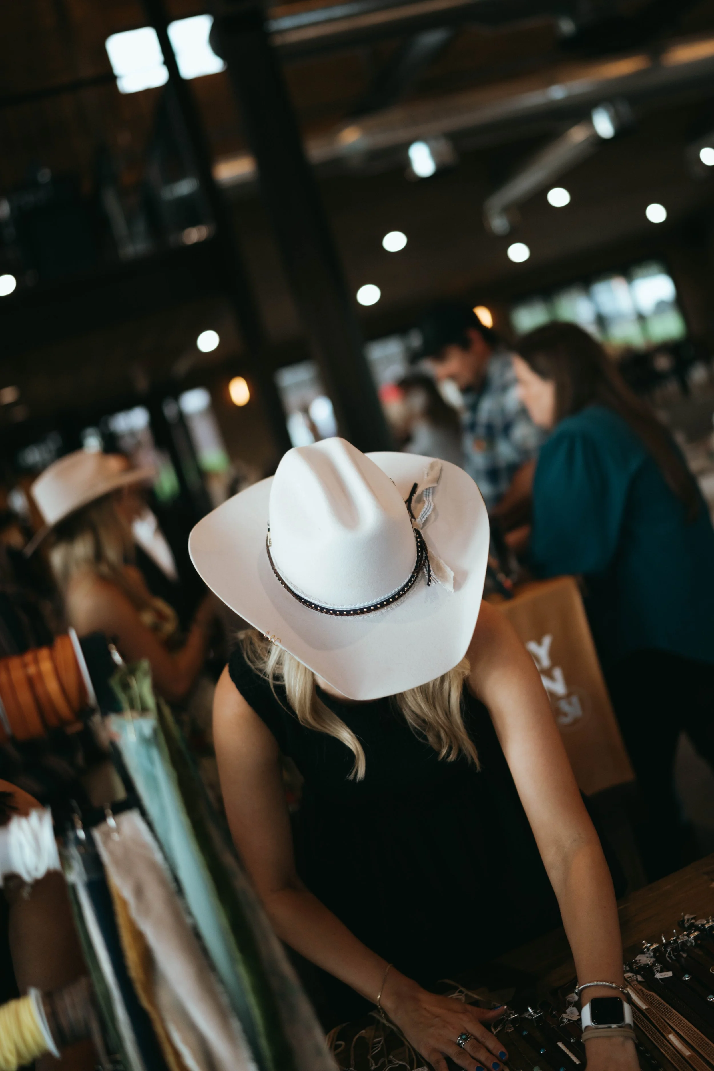 A woman sorts hat bands while wearing a silver belly cattleman hat and gets ready to make hats for guests.