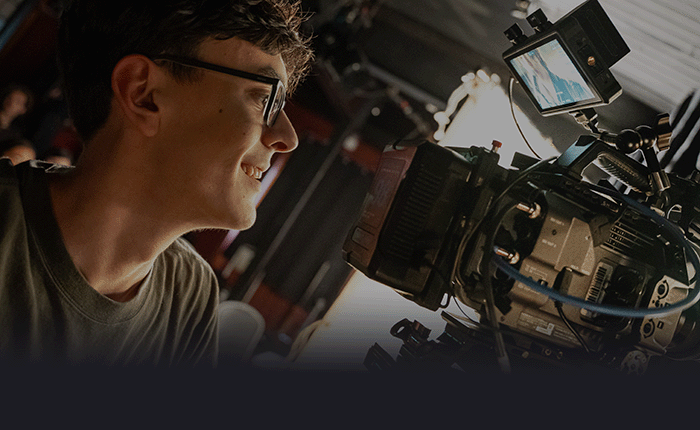 Jeune homme regardant un caméscope en studio avec un sourire, équipé d'une caméra professionnelle et d'un moniteur