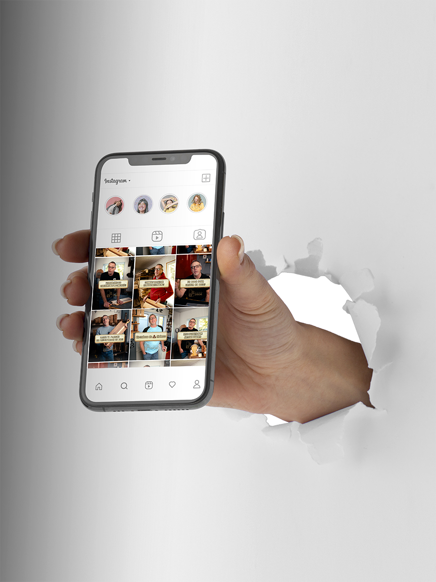 Main tenant un smartphone affichant plusieurs photos Instagram, sorti d’un trou dans un mur blanc.