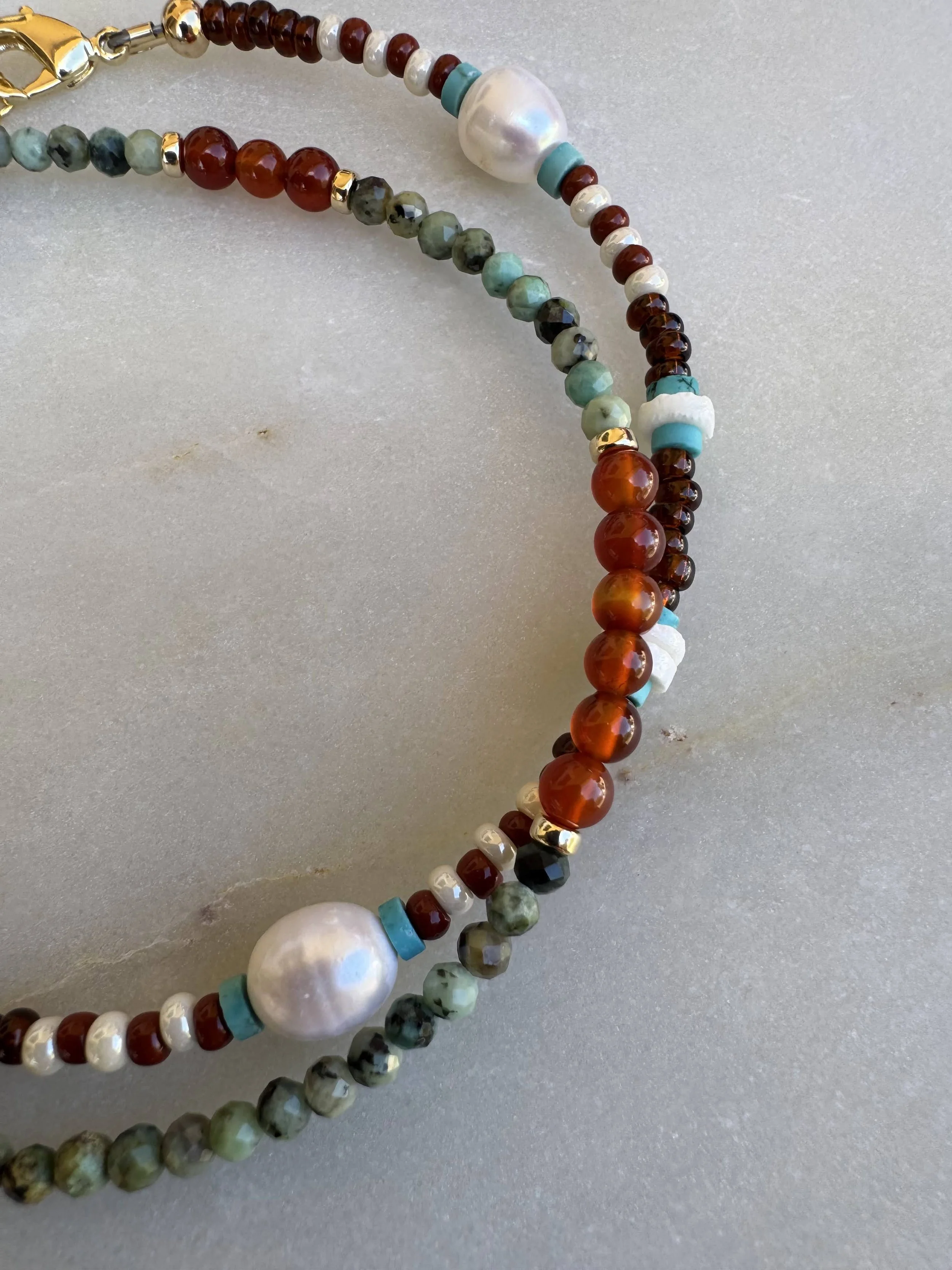 Colorful beaded necklaces with various sizes and shapes of beads, including turquoise, red, white, black, and metallic accents, on a neutral surface.