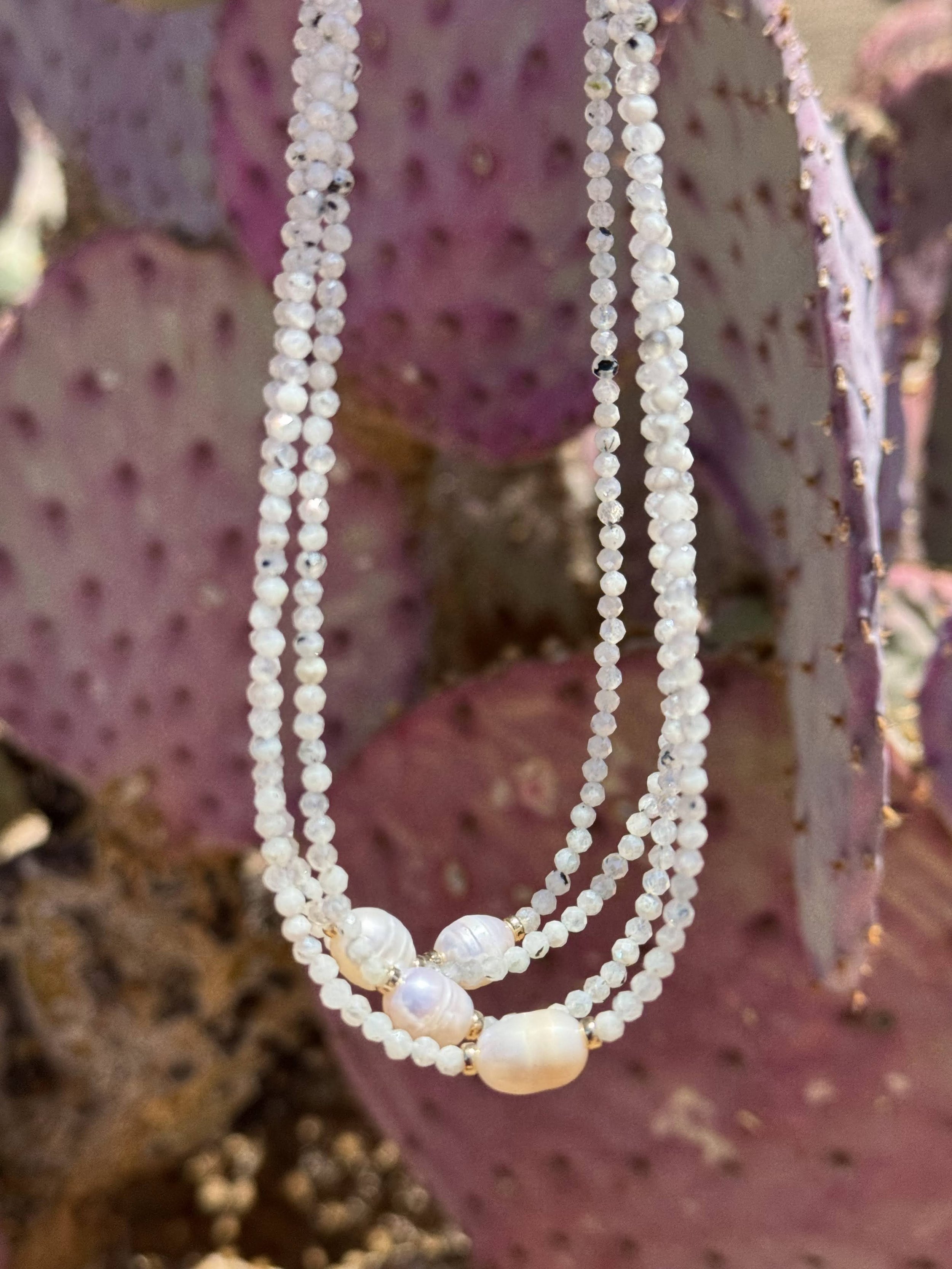 Three strands of white pearl necklaces hanging in front of purple prickly pear cactus.