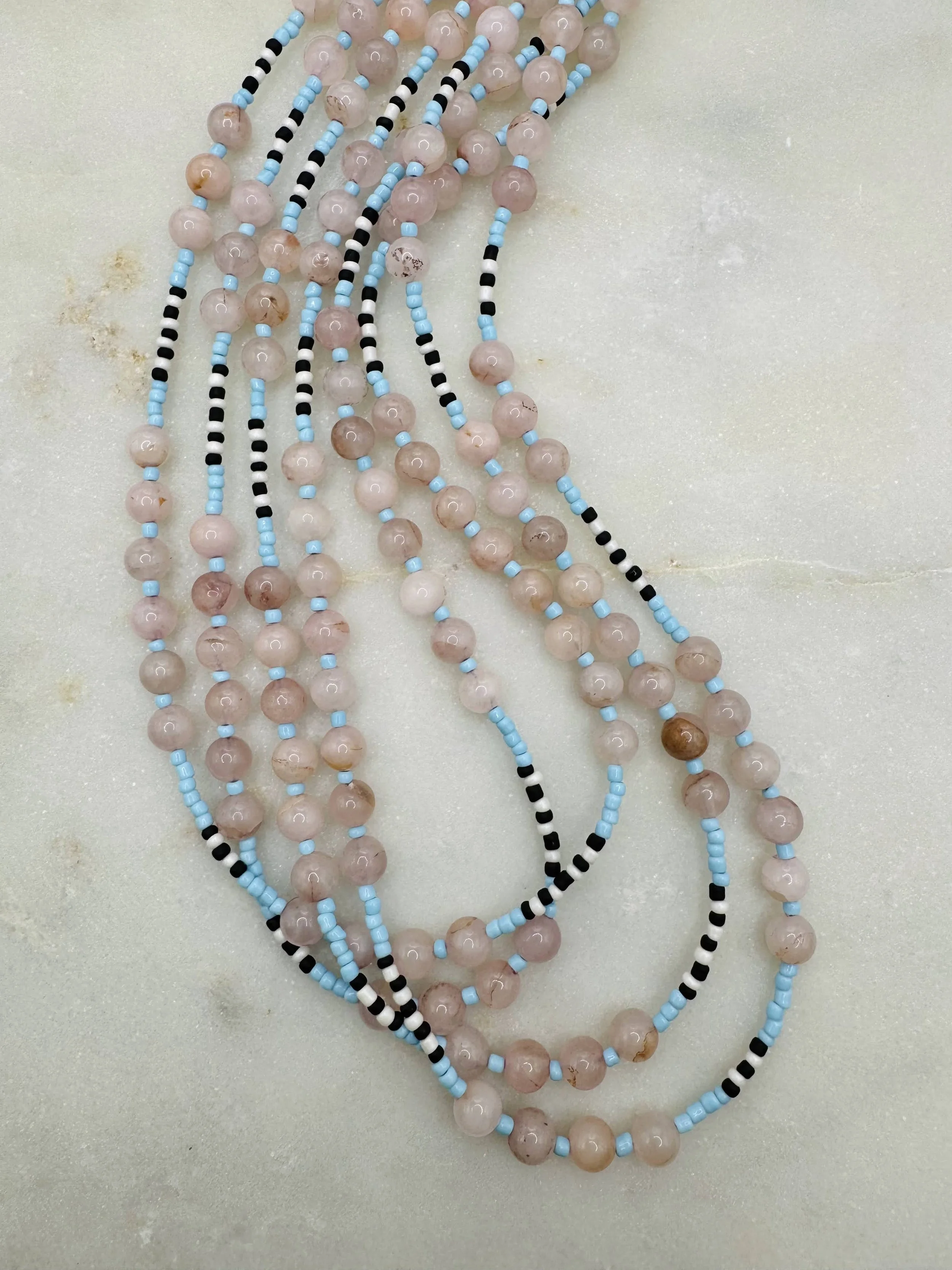 Multiple strands of beaded necklaces with pink, black, white, and blue beads are displayed on a light-colored surface.