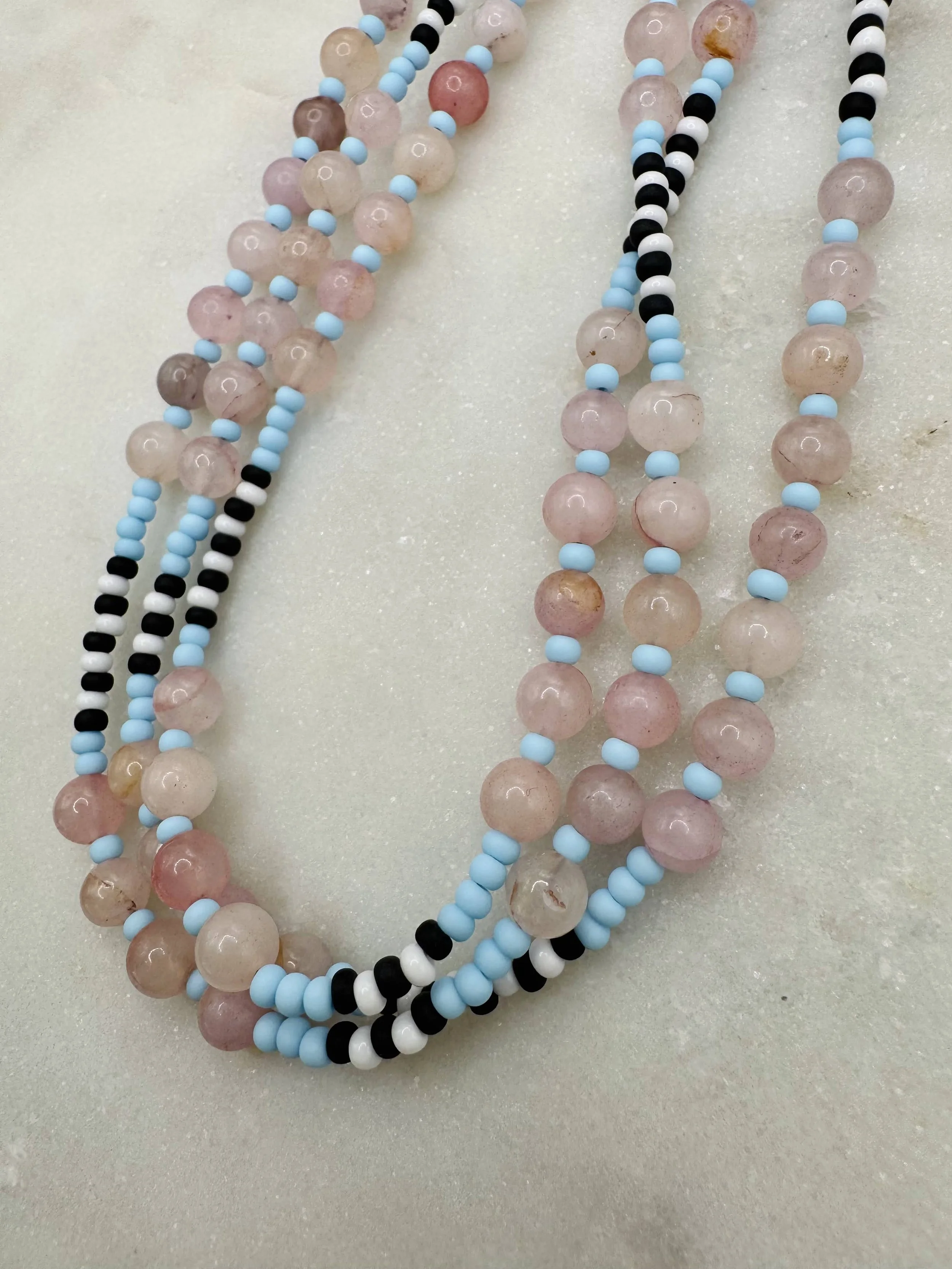 Multiple strands of beaded necklaces with pink, black, white, and blue beads are displayed on a light-colored surface.