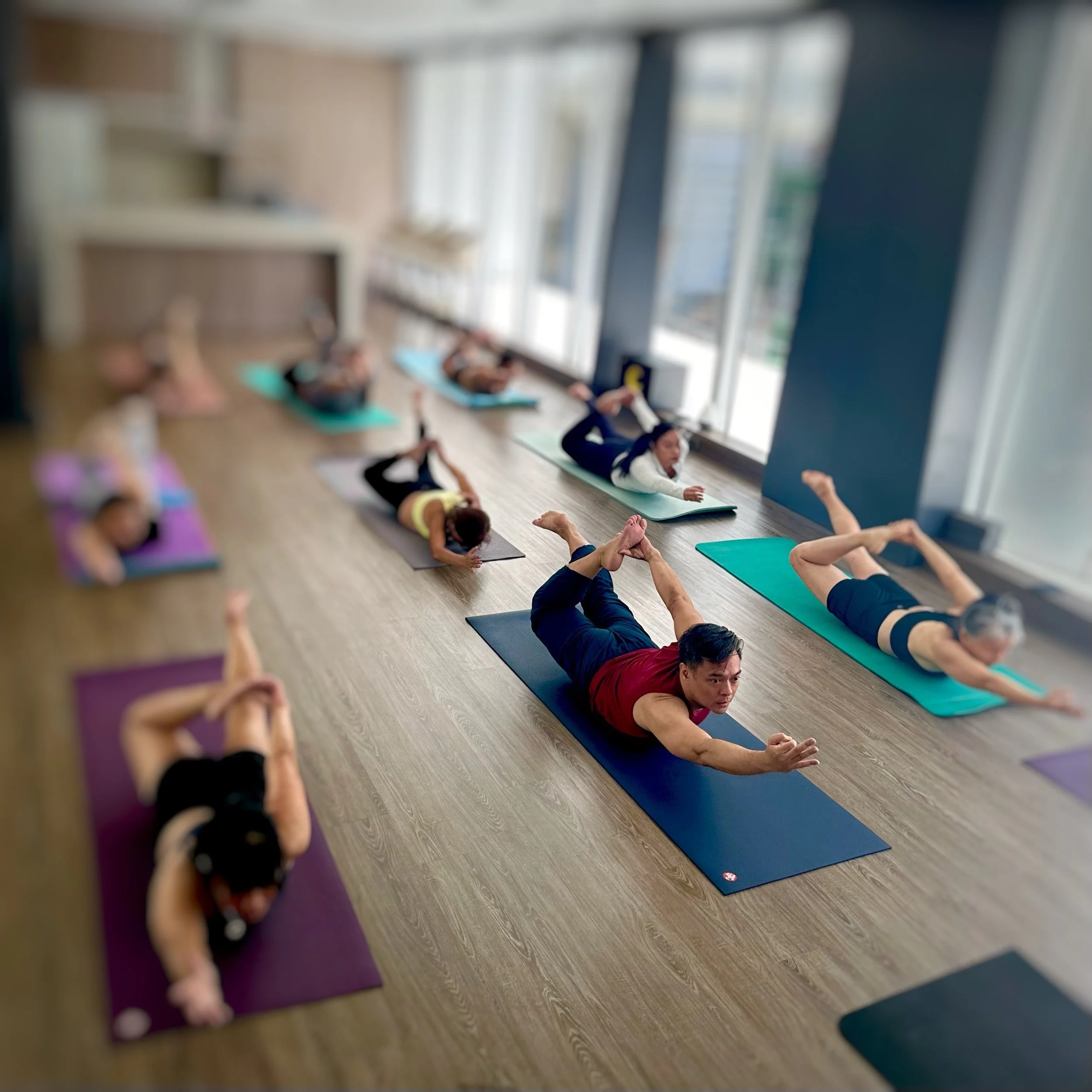 Group of people participating in a yoga class at the StudioM community center using colorful yoga mats on a sunny morning.