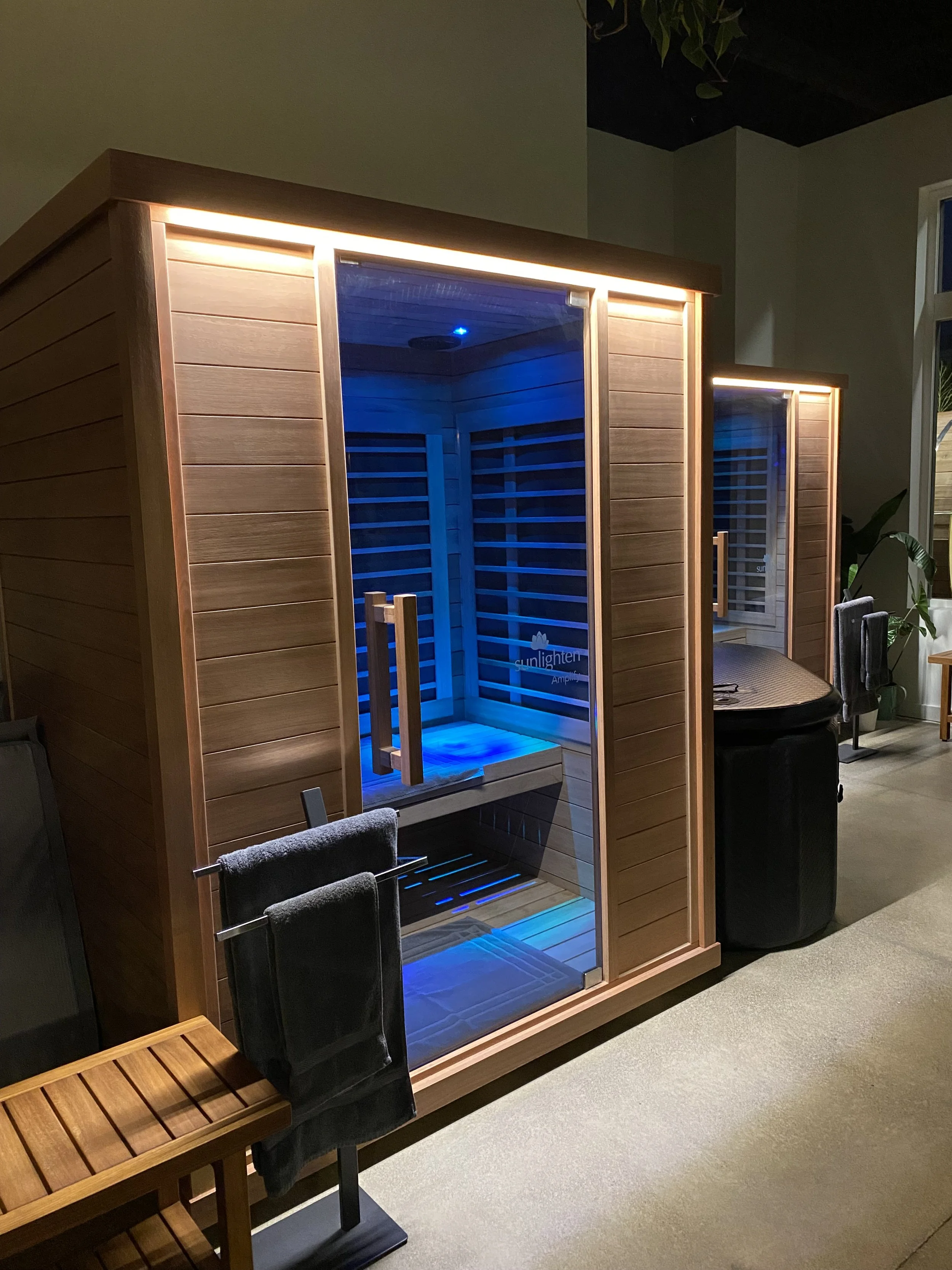 Indoor infrared sauna with wooden exterior, glass door, blue LED lighting, and a bench inside.