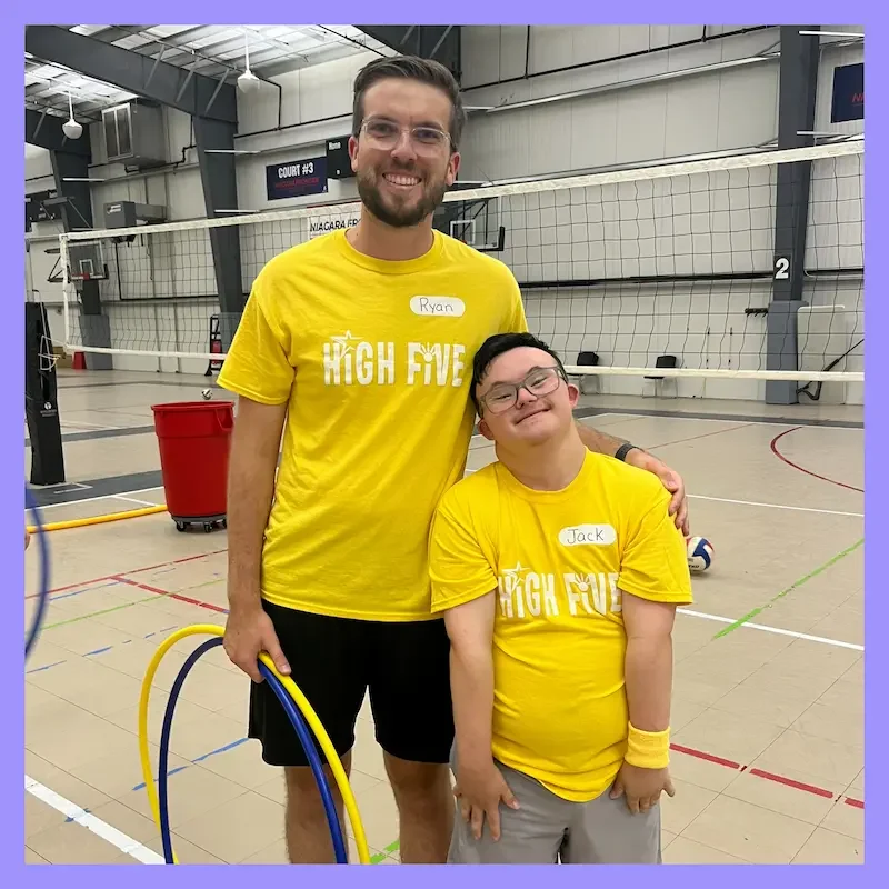 The Champion Project of Western, New York, High Five volunteer and participant smile together in a gym while holding hula hoops, wearing matching yellow shirts