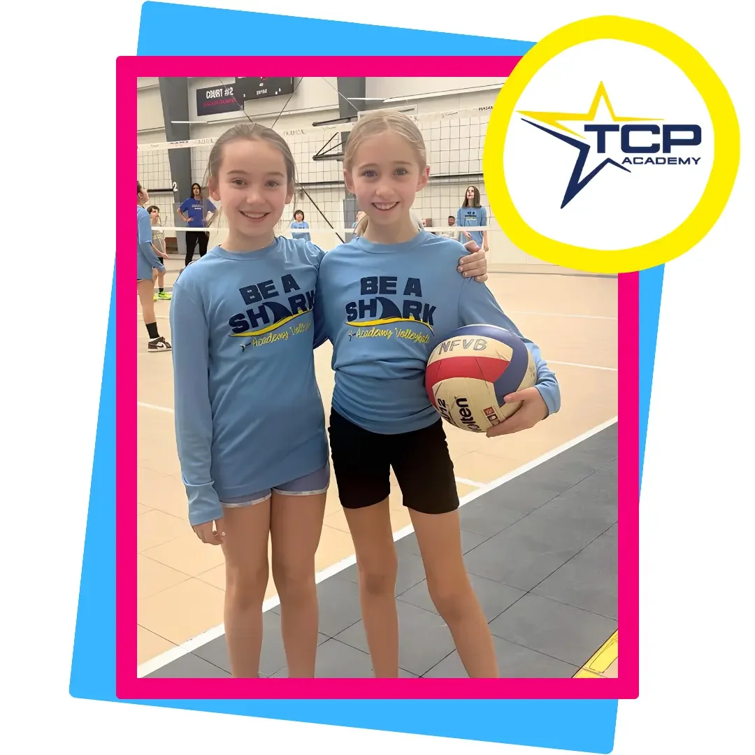 Two smiling girls in ‘Be A Shark’ shirts pose with a volleyball at TCP Academy, highlighting youth volleyball training, friendship, and skill development in a fun, supportive environment