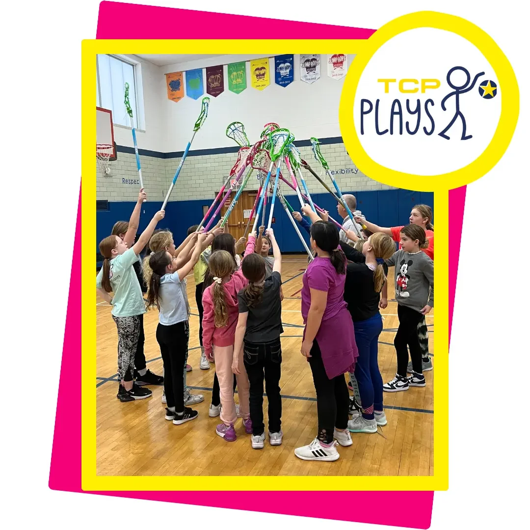 Group of girls raising lacrosse sticks in unison during a TCP Plays indoor gym session, promoting teamwork, youth engagement, and inclusive sports through active play