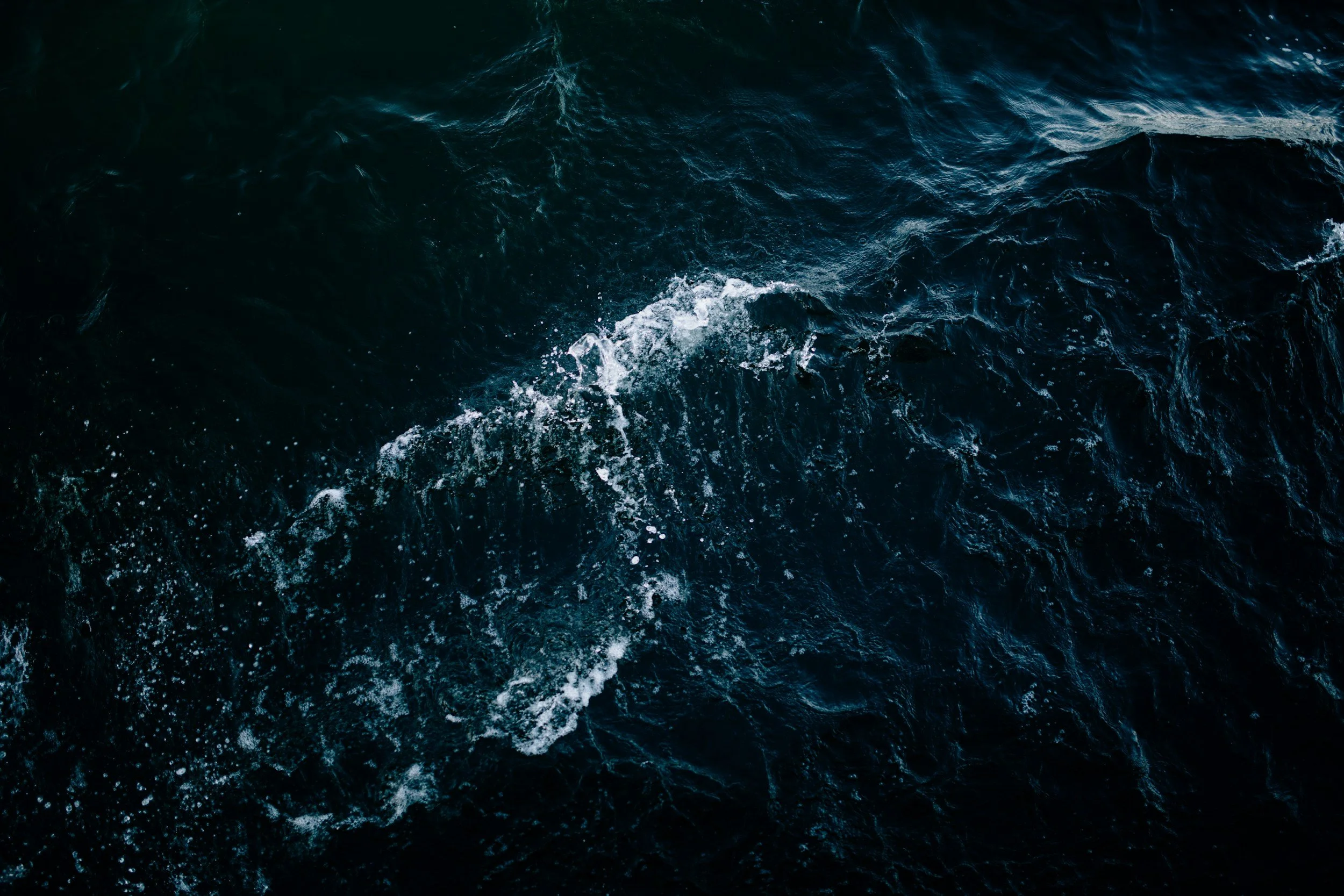 Aerial view of dark blue ocean water with white foam and waves.