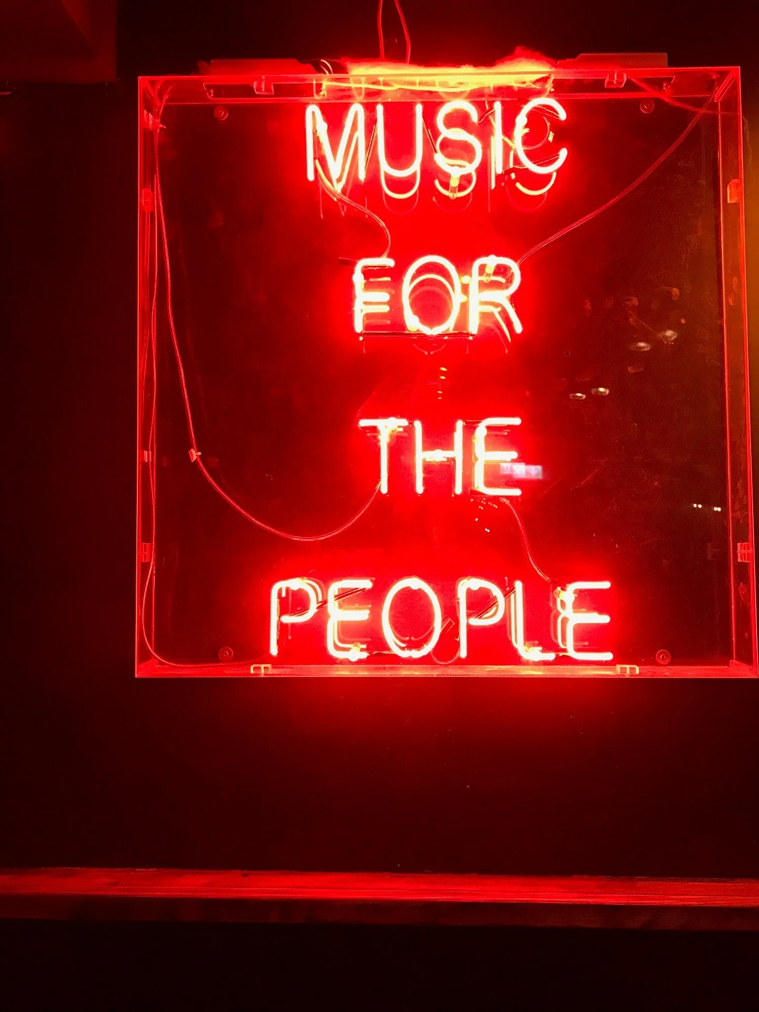 Red neon sign that reads 'Music for the People' on a dark wall.