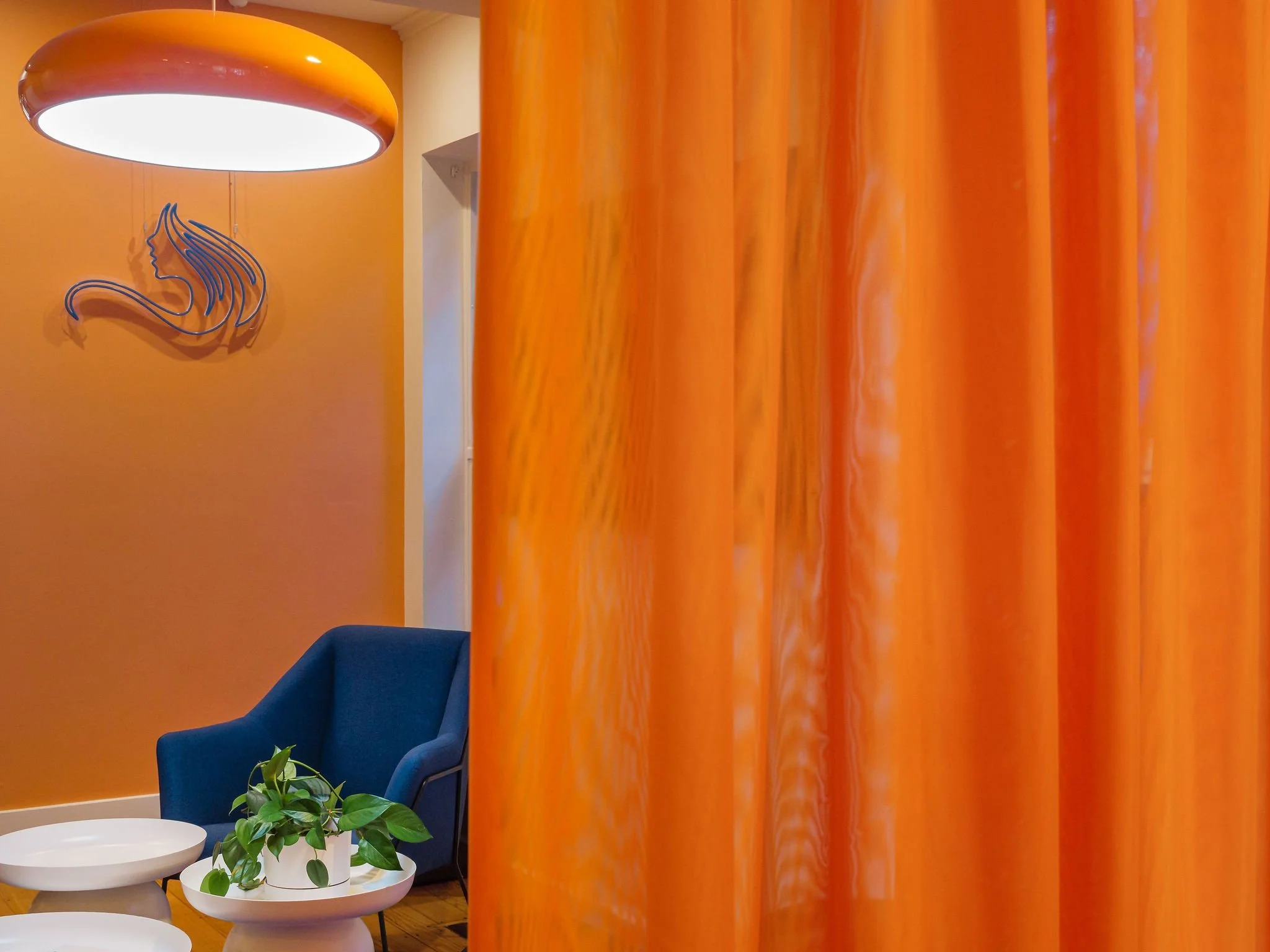 View of orange curtain, with blue armchair in background. Commercial interior design to liven and refresh space to meet practical needs.